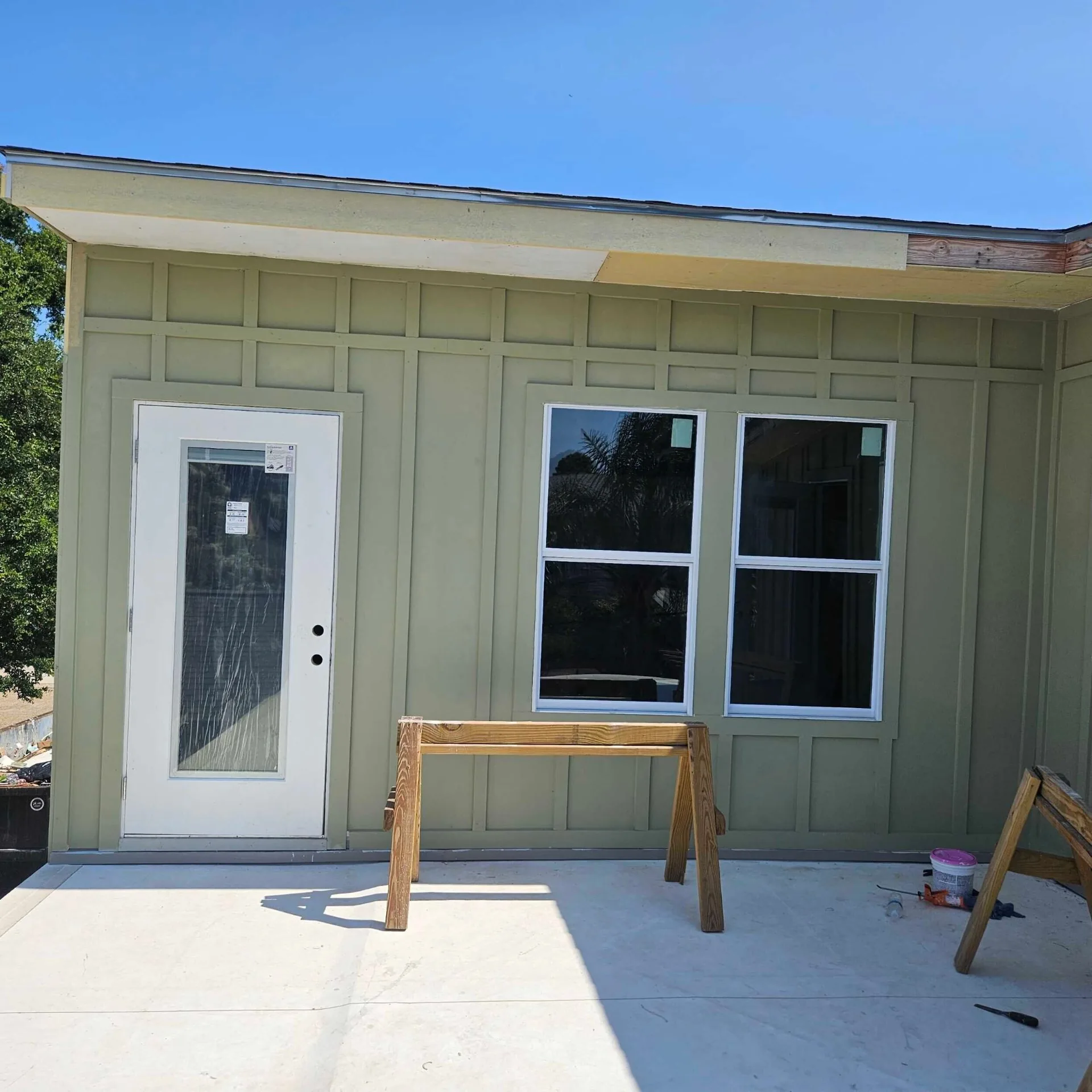 Finished green board-and-batten siding on rear addition at Blanke Street Metairie home with new single-lite door and double-hung windows installed