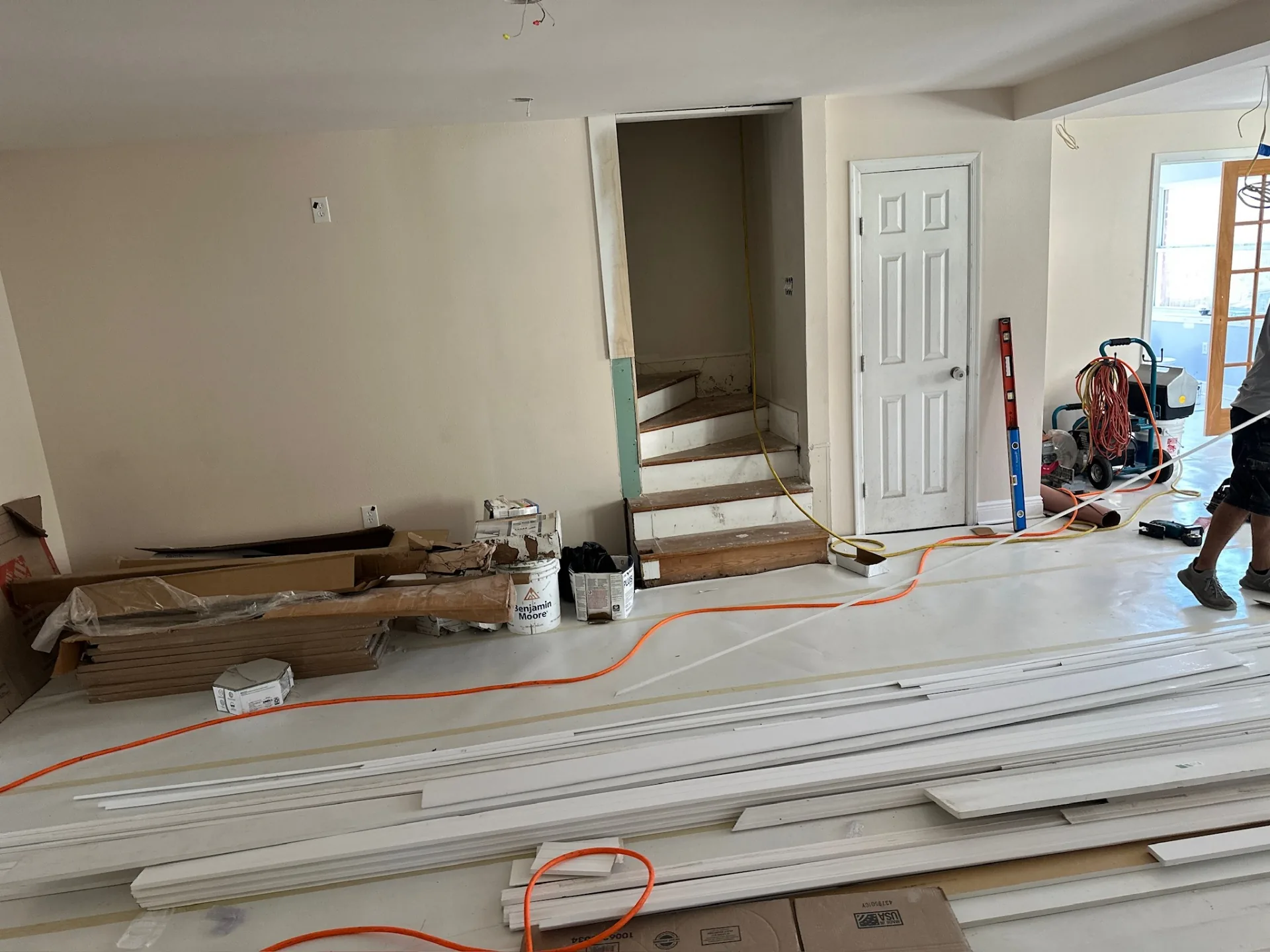 Interior stair opening at Blanke Street Metairie home during finish phase, with rosin-papered floor, staged white trim stock, and materials laid out for flooring around the staircase