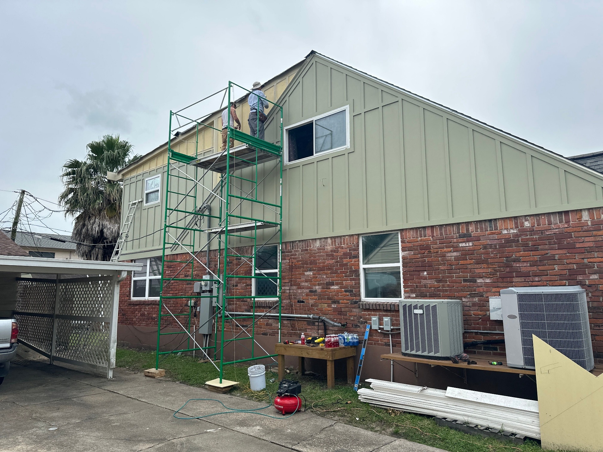 Crew on scaffolding painting new board and batten siding on rear gable of Blanke Street Metairie whole-home remodel