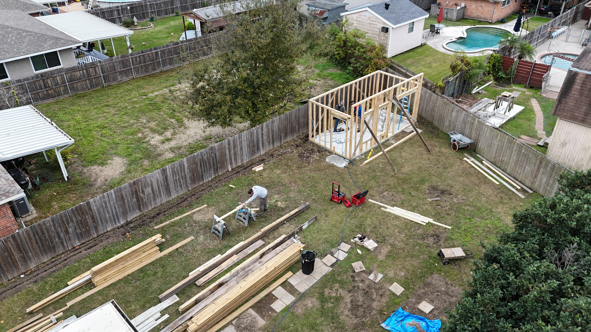 Aerial backyard context drone shot of Cajun Home Services crew framing Hardie-siding shed in Metairie Louisiana