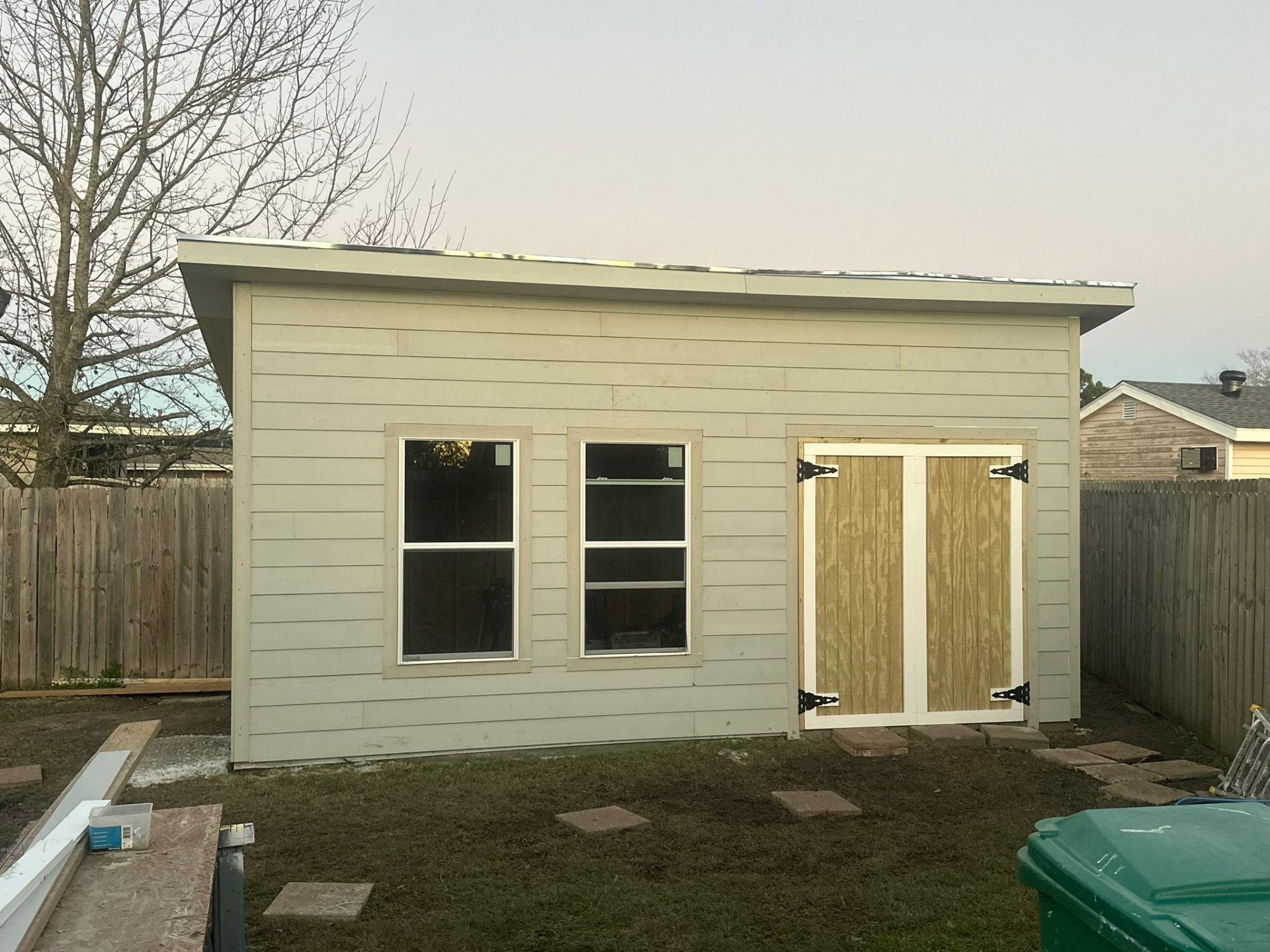 Metairie shed with full Hardie plank siding in primer coat and freshly built pressure-treated barn doors hung but not yet stained