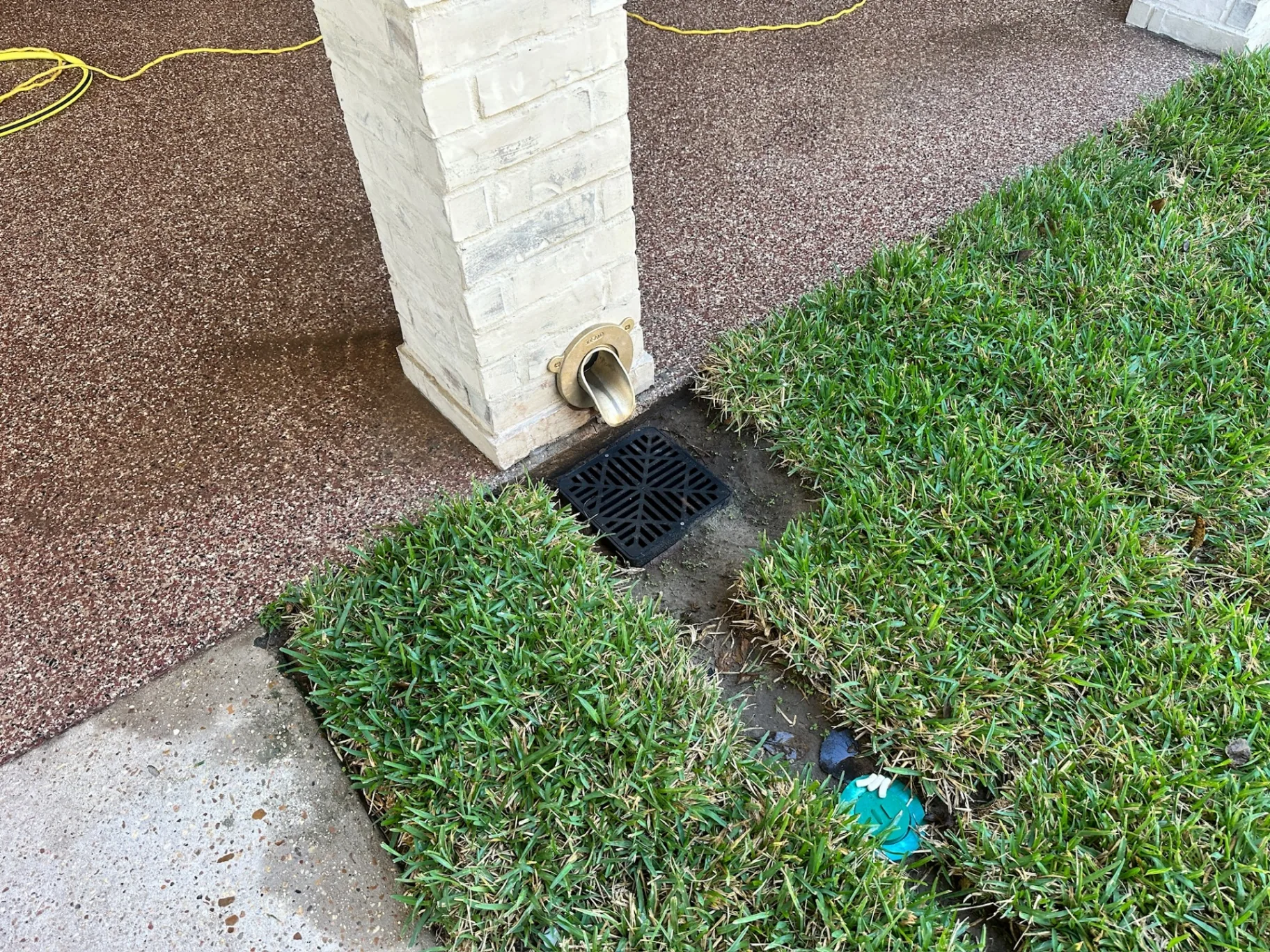 Finished limewashed brick patio post with brass hidden downspout scupper draining into black area drain grate at Destrehan Louisiana home by Cajun Home Services