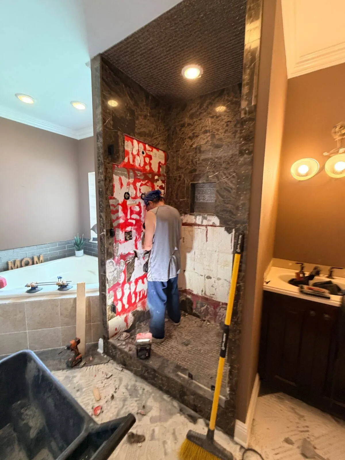 Cajun Home Services crew applying RedGard waterproofing membrane to shower walls over marble tile surround during master bath remodel in Destrehan Louisiana