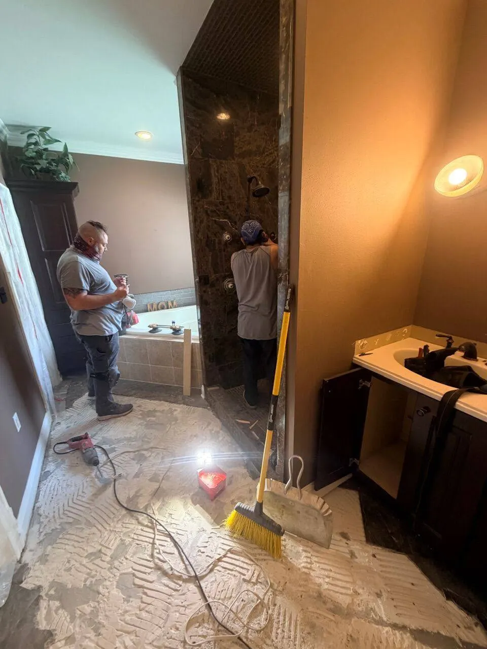 Cajun Home Services crew prepping mortar and demoing tile inside master bathroom with halogen work light and tub visible during Destrehan LA remodel