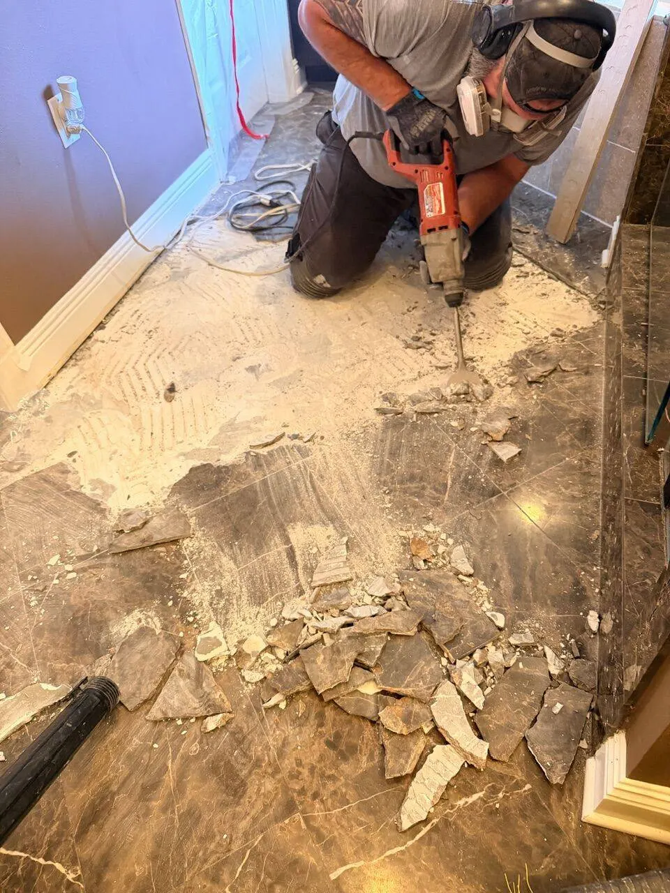 Cajun crew member in respirator using rotary hammer to break up old marble floor tile during master bath demolition in Destrehan Louisiana
