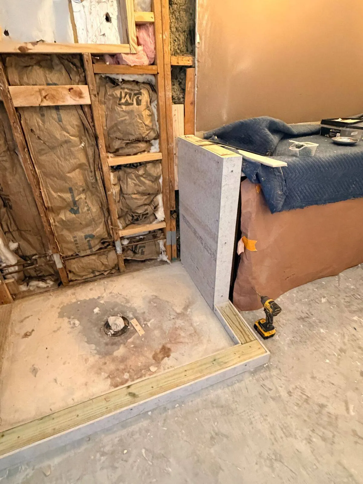 New pressure-treated shower curb framing and cement board installation over concrete slab with exposed insulation behind during Destrehan LA master bath rebuild