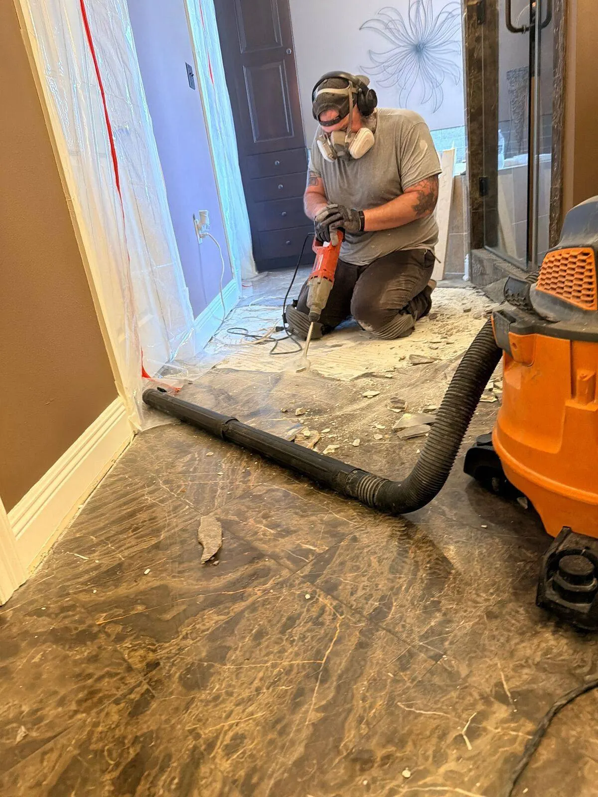 Cajun Home Services crew member using rotary hammer with dust extraction vacuum to remove old marble floor tile during master bath remodel in Destrehan LA