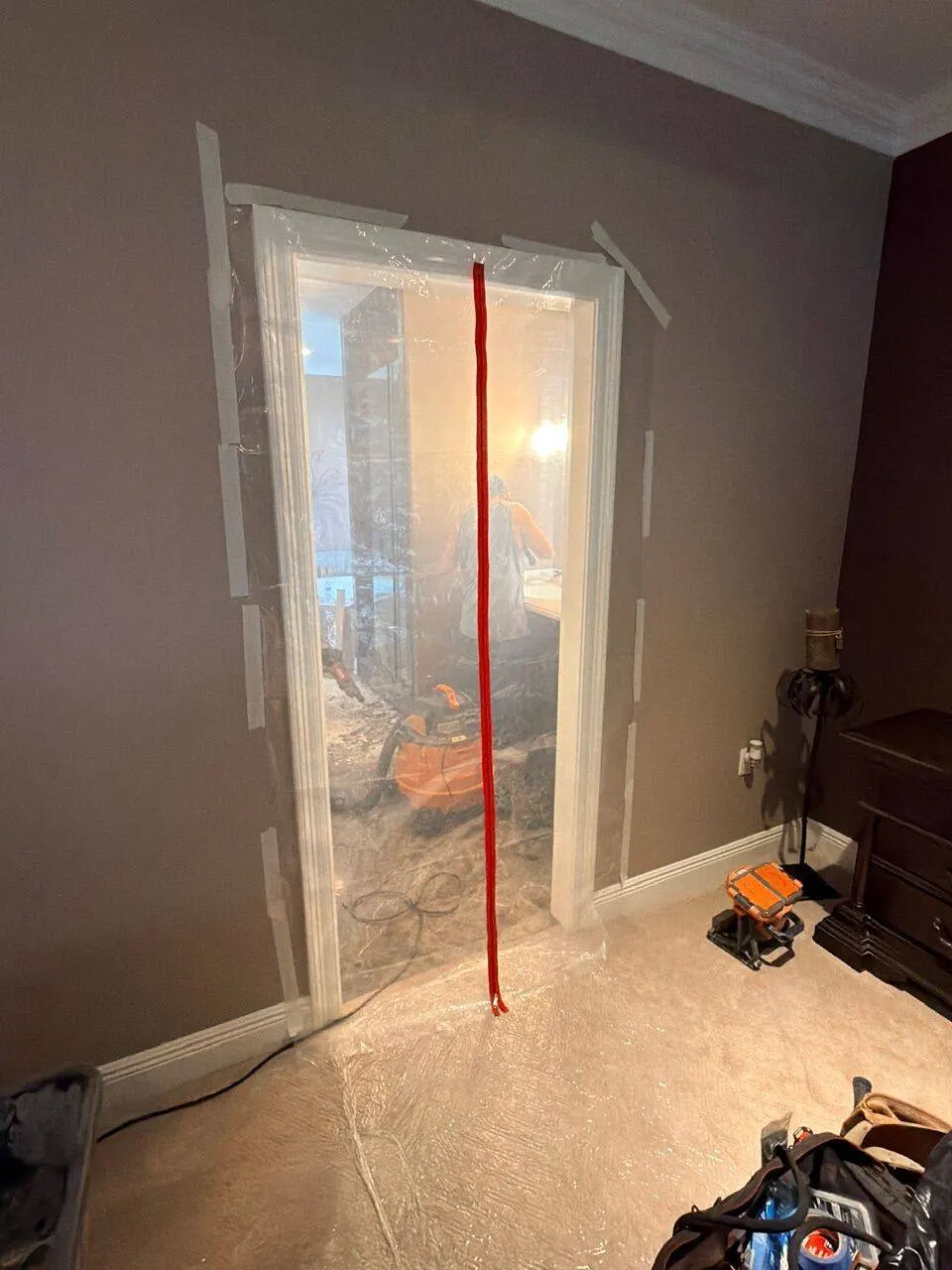 Zippered plastic doorway containment with red zipper isolating master bathroom from bedroom during dust control on Destrehan LA remodel