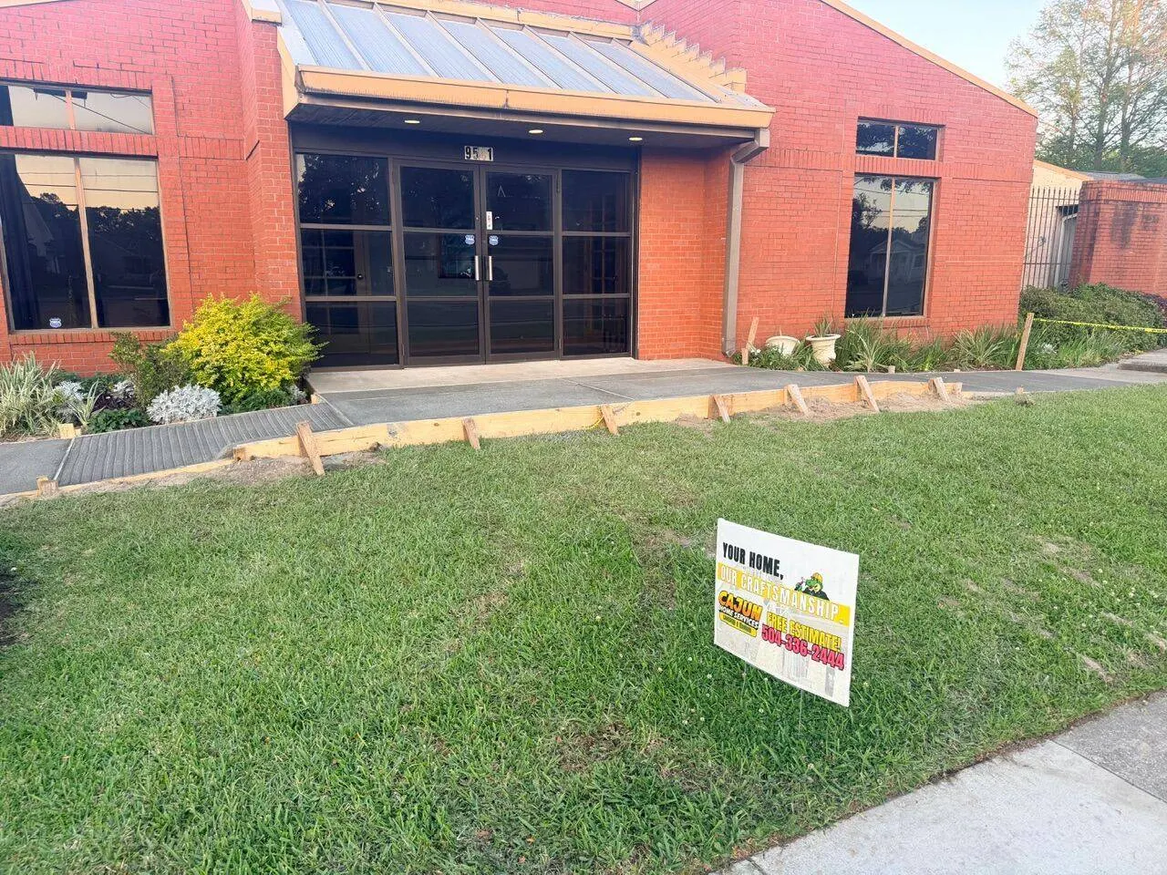 Completed commercial concrete walkway with formed expansion joints leading to Family Dentistry office entrance in River Ridge Louisiana with Cajun Home Services yard sign