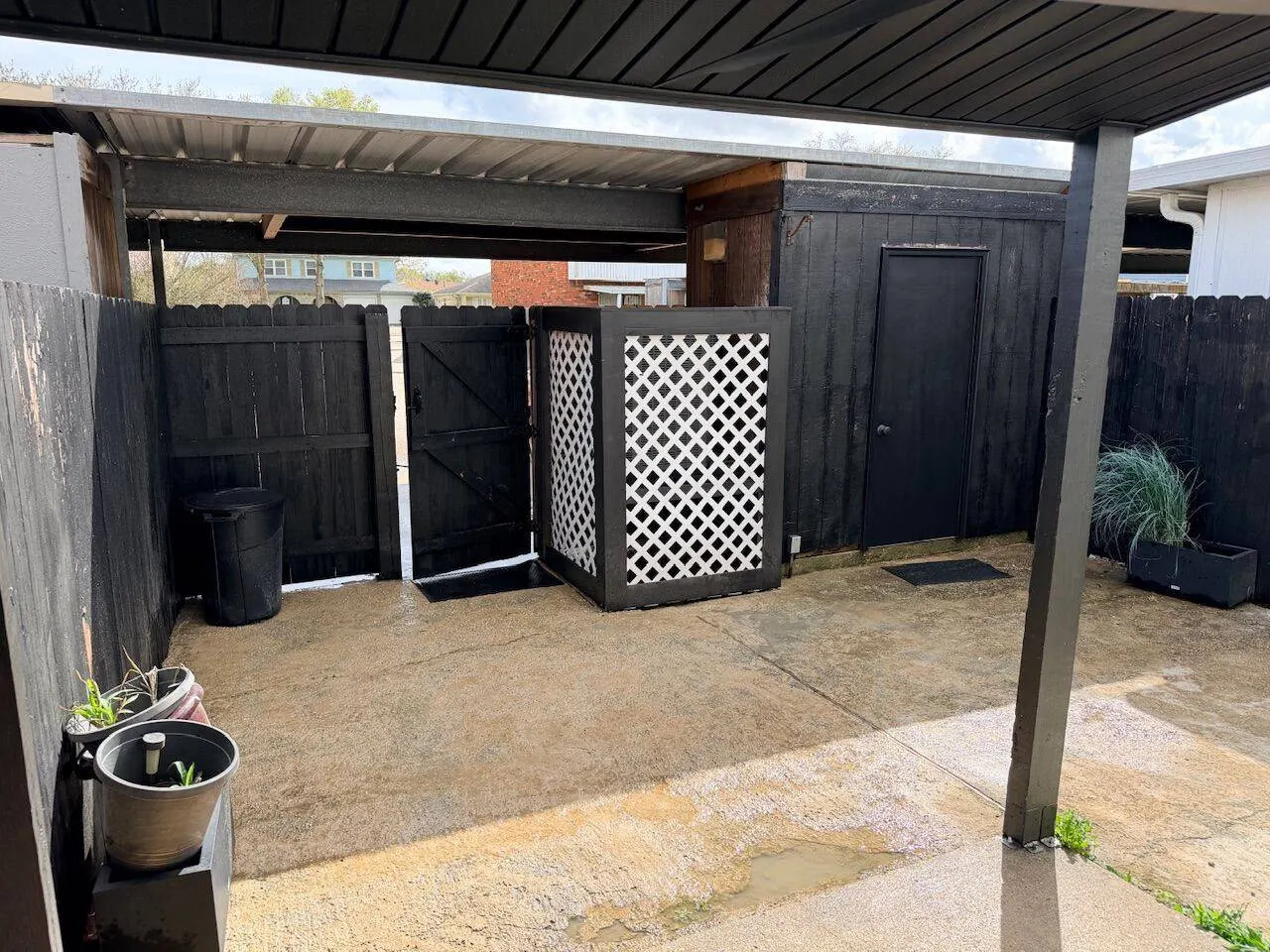Covered carport with black privacy fence and custom lattice AC unit cover at residential property in Metairie