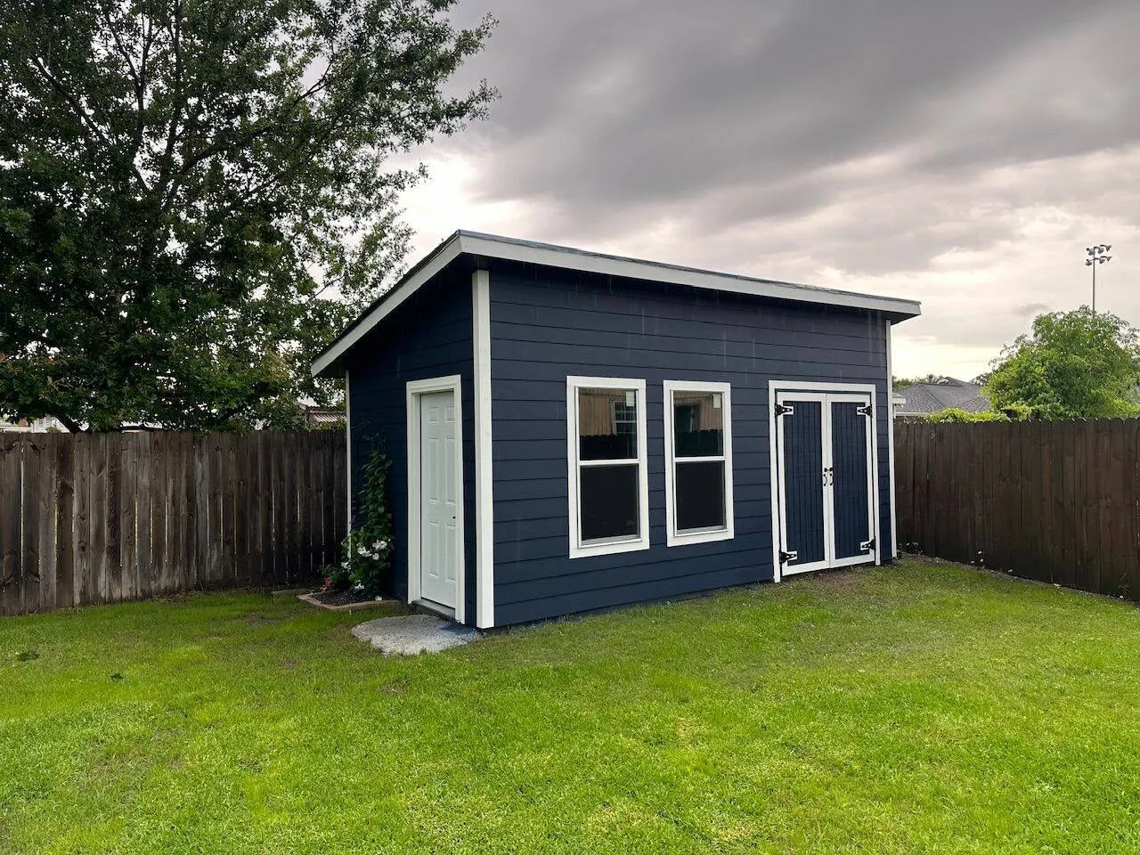 Completed backyard shed with navy siding and white trim in Metairie Louisiana