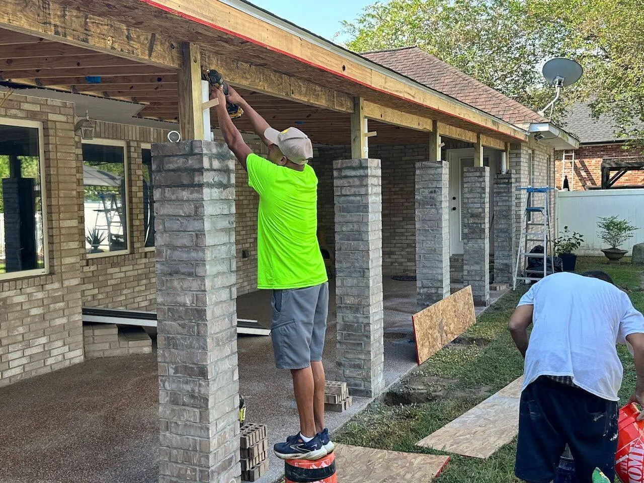 Crew member fastening patio cover framing with drill on brick column patio addition in Louisiana