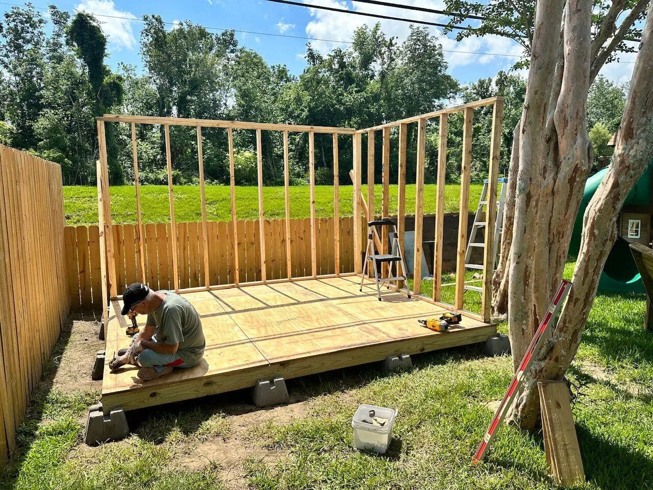 Crew member framing shed wall on plywood subfloor with pier block foundation in Southeast Louisiana backyard