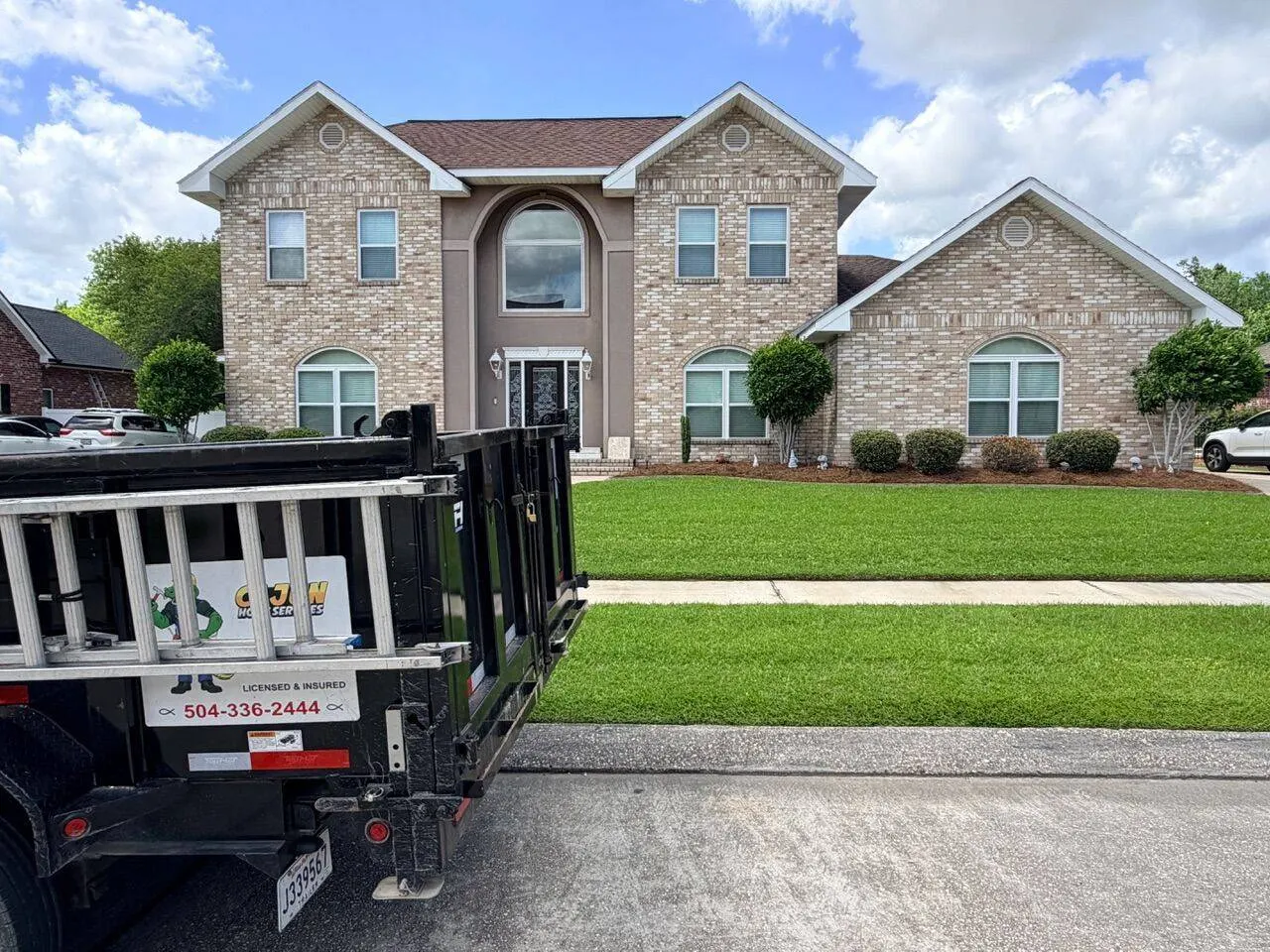 Two-story brick and stucco home exterior in Destrehan Louisiana with Cajun Home Services dump trailer parked in front during master bathroom remodel project in St. Charles Parish