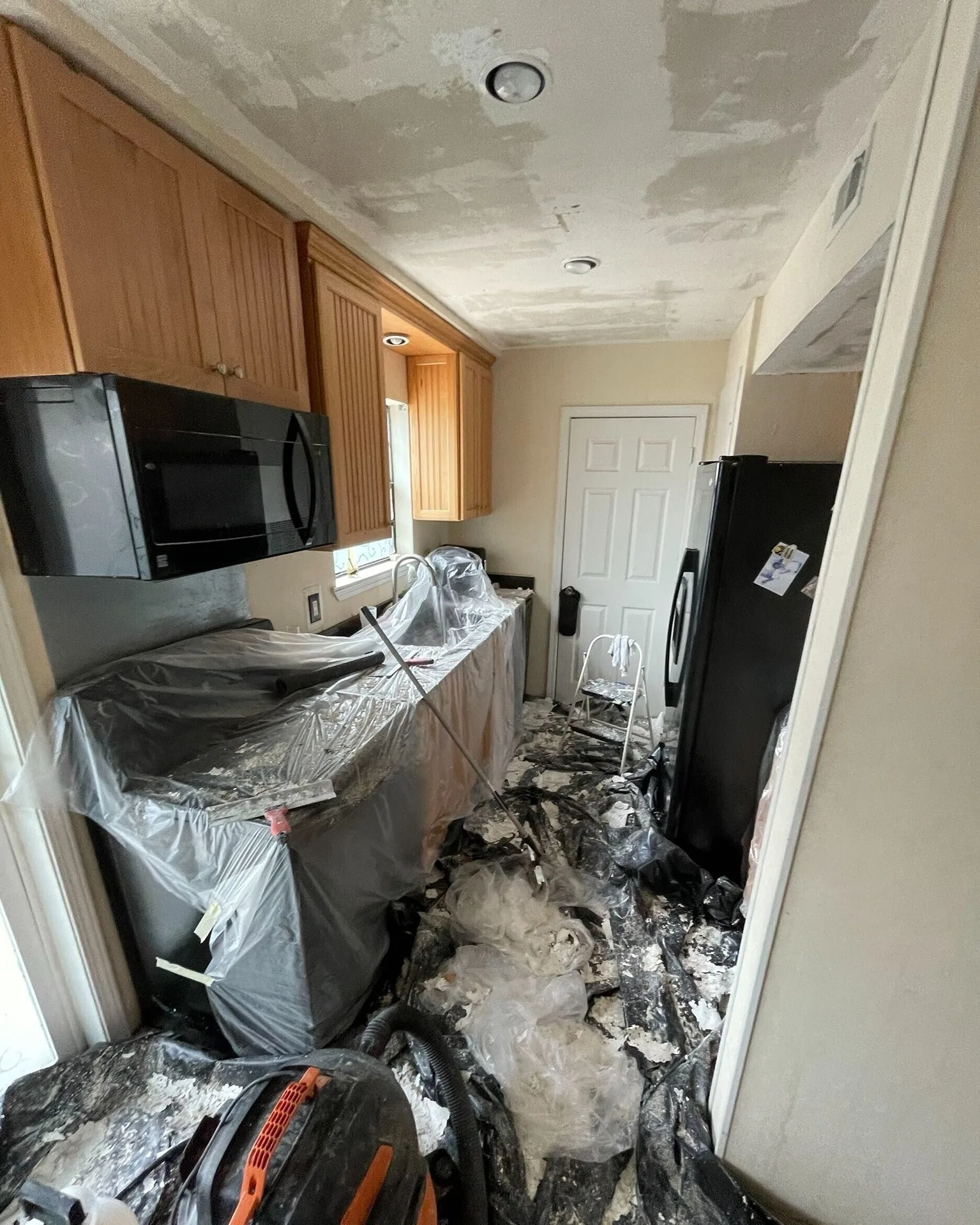 Gretna LA kitchen during popcorn ceiling removal with plastic sheeting protecting cabinets and countertops, debris and dust mitigation in progress by Cajun Home Services interior remodel crew