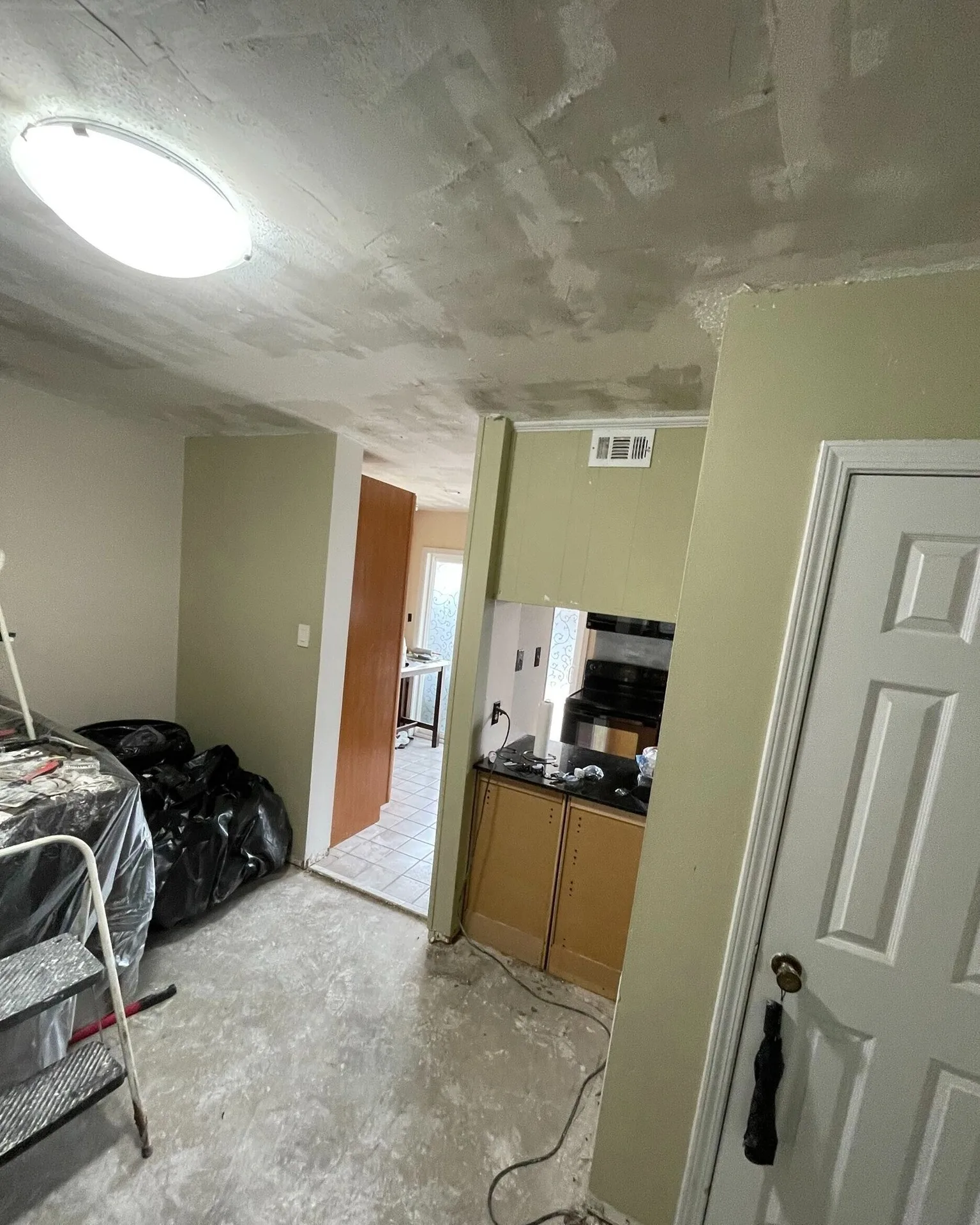 Gretna LA hallway and dining nook mid-remodel with freshly skim-coated ceiling drying, plastic-covered furniture and stepladder staged for next paint phase by Cajun Home Services