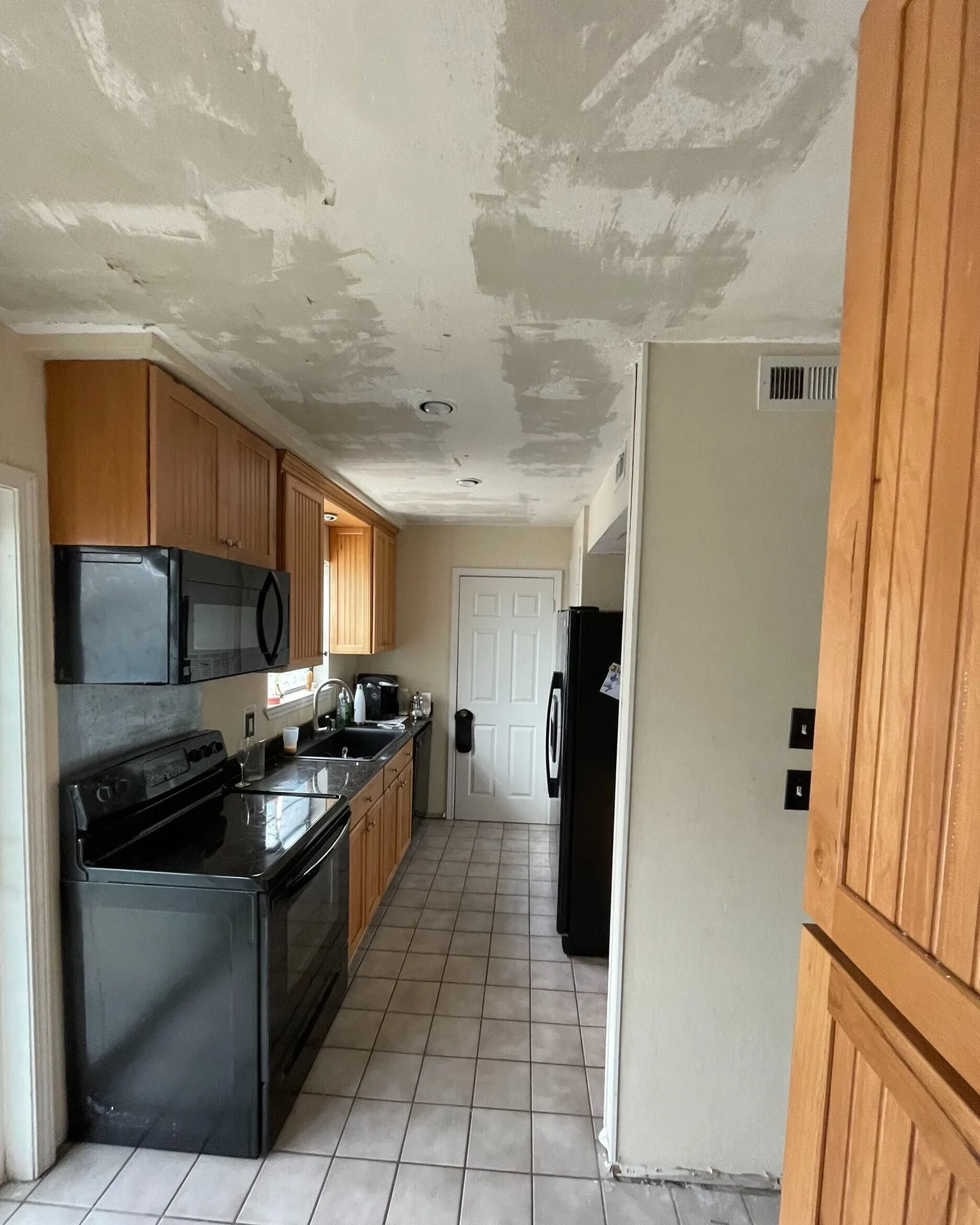 Gretna LA galley kitchen mid-remodel with popcorn ceiling fully scraped and skim-coated, original oak cabinets and black appliances in place before paint and trim phase by Cajun Home Services