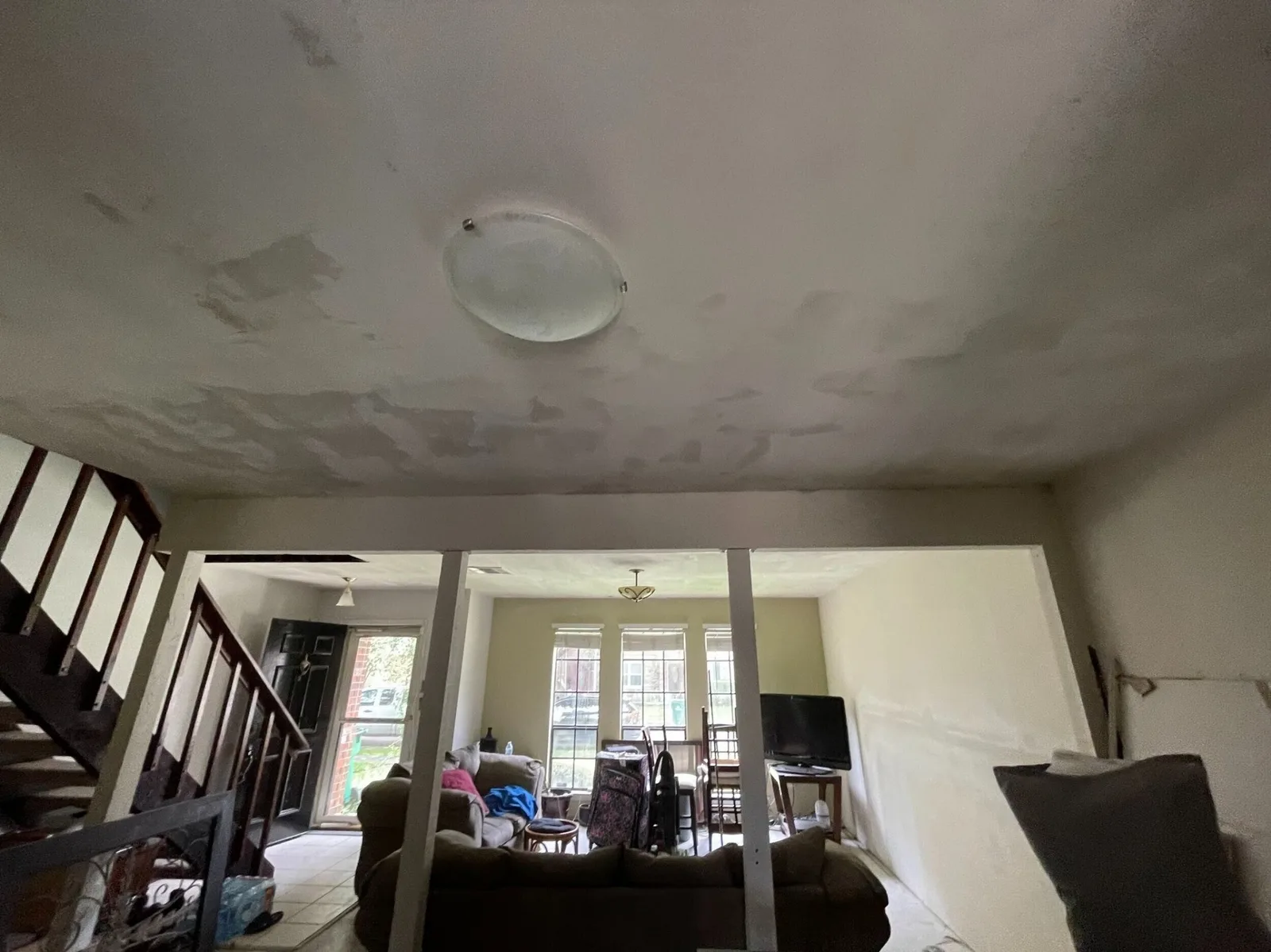 Gretna LA two-story living room interior wide shot with patched and floated ceiling, staircase on left and bay windows in background — mid-remodel by Cajun Home Services