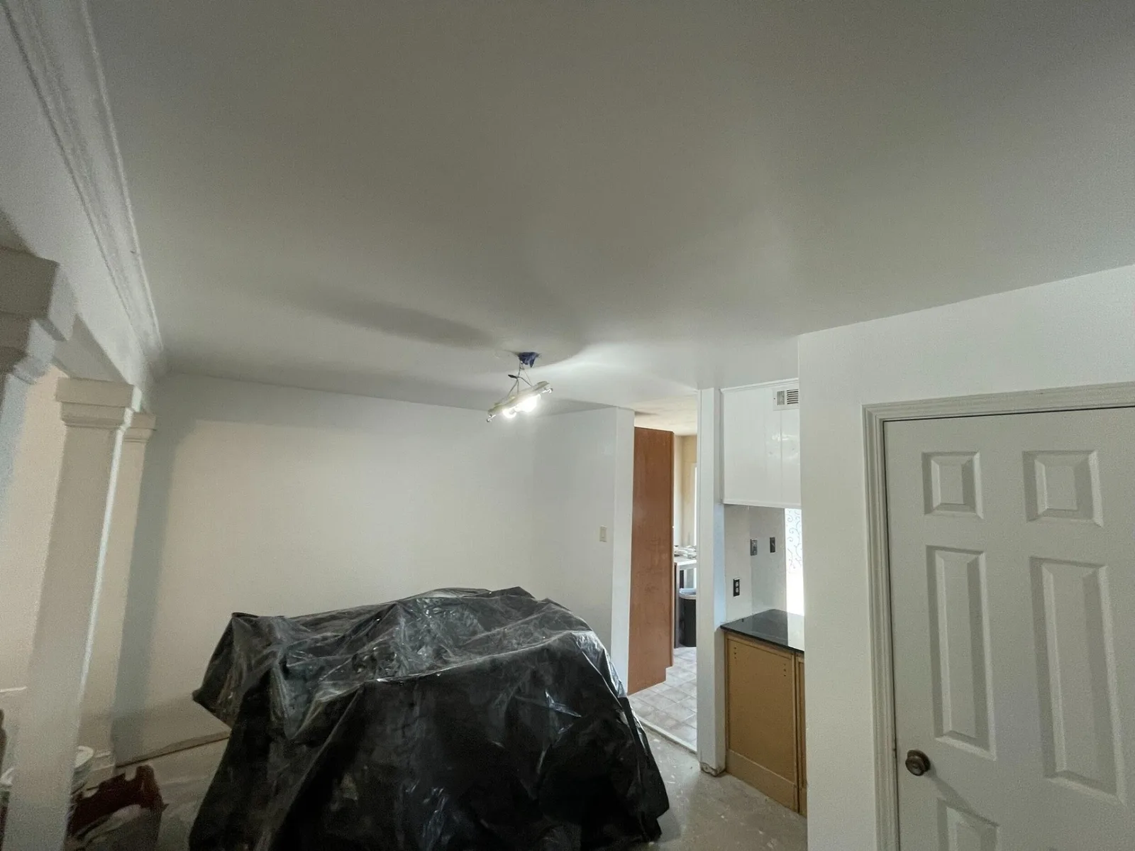 Gretna LA dining area with freshly skim-coated and primed ceiling smooth and ready for paint, custom column trim and crown moulding visible at left, furniture covered in black plastic during Cajun Home Services interior remodel
