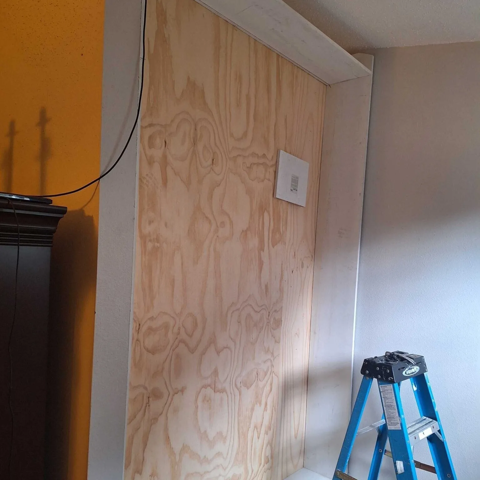 Gretna LA living room accent wall framed and clad in raw plywood backing for custom built-in shelving unit, prepped against original gold accent wall before trim and paint by Cajun Home Services
