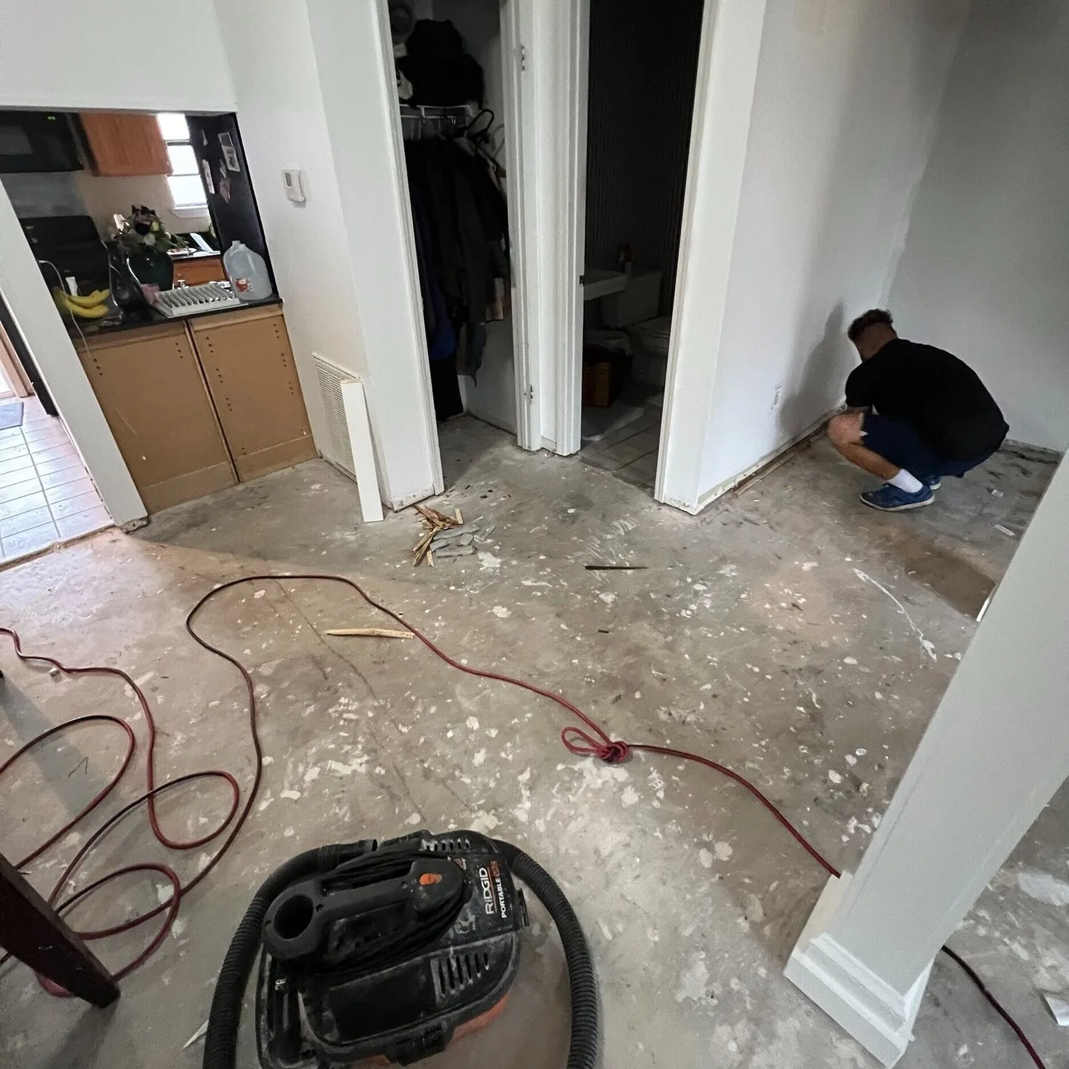 Gretna LA hallway with old flooring fully removed showing bare concrete slab, Cajun Home Services crew member inspecting baseboard transitions near bathroom and closet before LVP installation