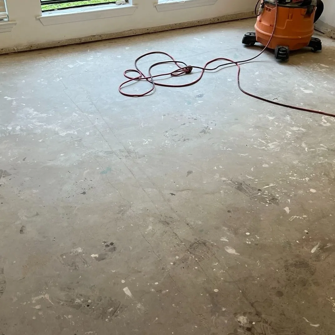 Gretna LA living room bare concrete subfloor swept and vacuumed clean, hairline cracks visible and ready for moisture barrier and luxury vinyl plank underlayment by Cajun Home Services