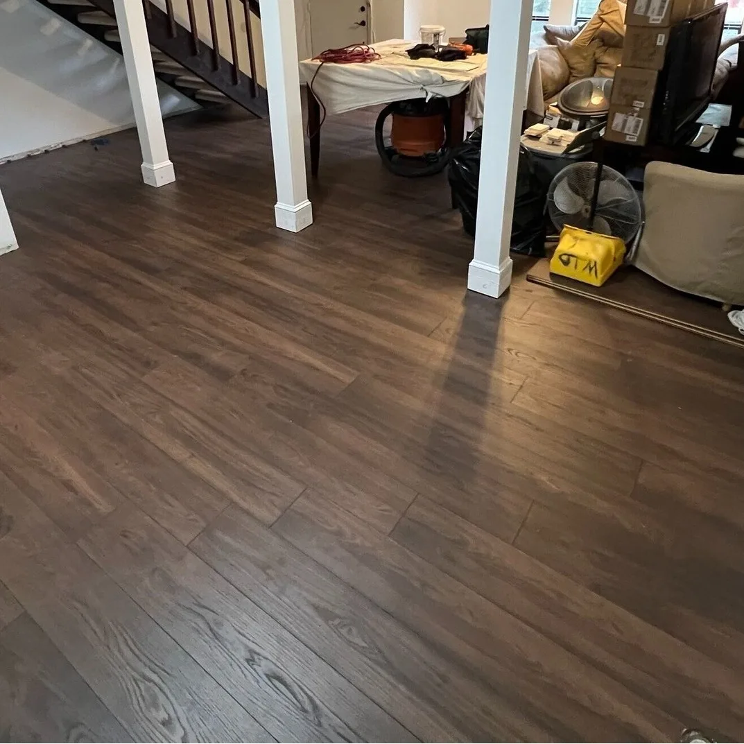 Gretna LA living and dining area with newly installed warm walnut luxury vinyl plank flooring fully laid wall to wall, white column wraps anchoring the open layout and staircase visible in background by Cajun Home Services