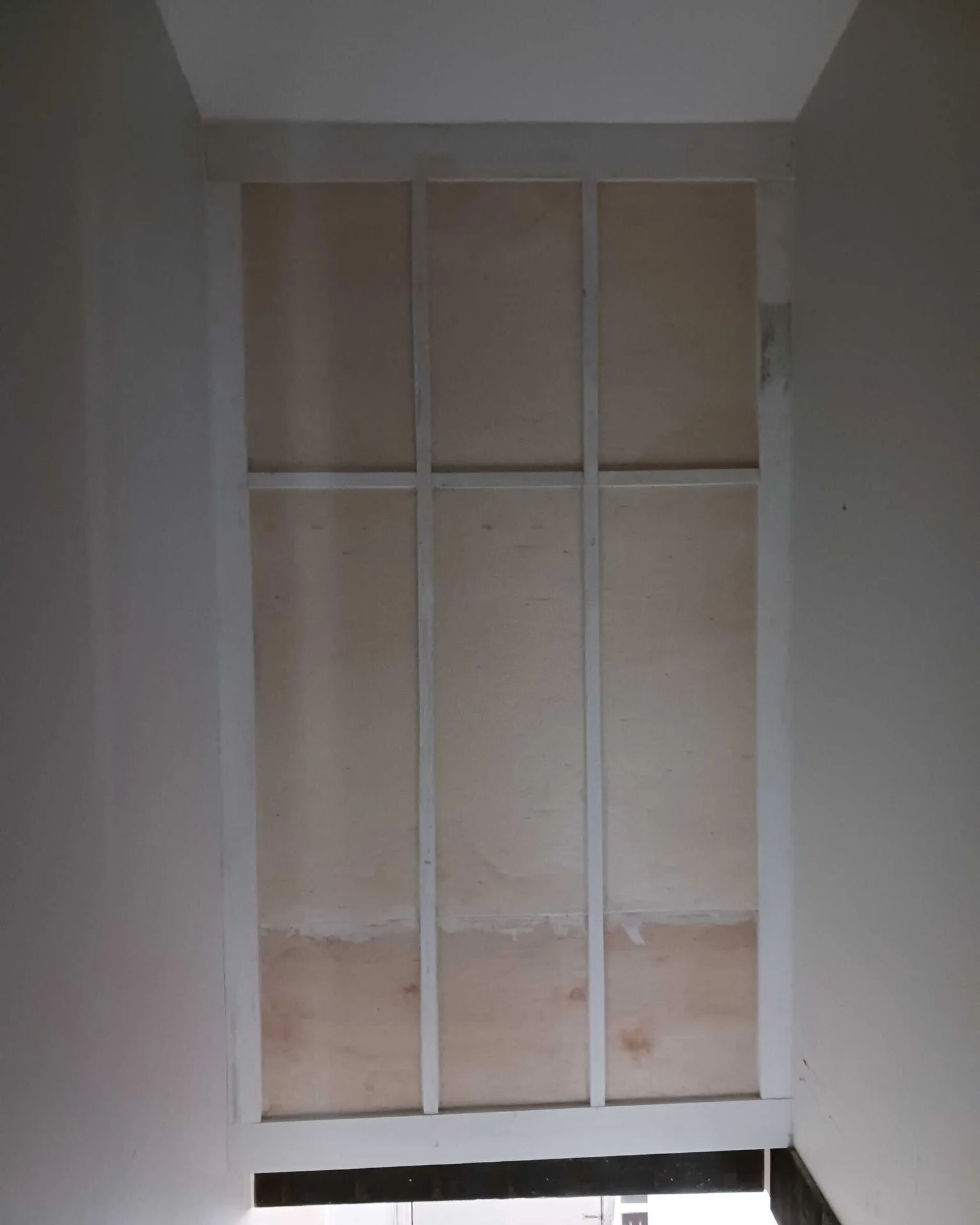 Gretna LA tall stairwell wall with custom board-and-batten trim grid installed in three vertical bays, primed white over plywood backing before final paint coat by Cajun Home Services carpentry team