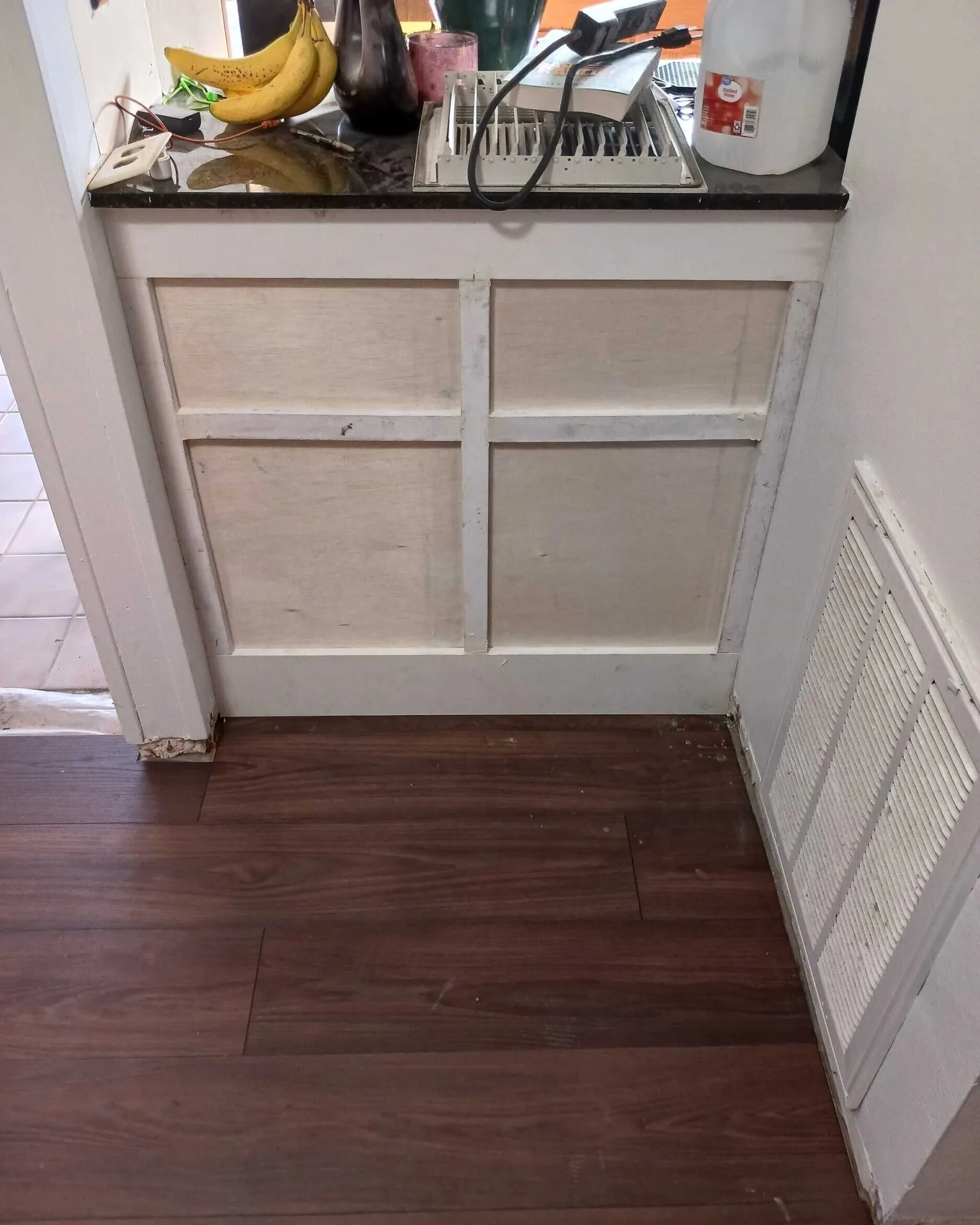 Gretna LA kitchen pony wall before custom board-and-batten upgrade, original four-panel raised pass-through cabinet beneath granite countertop and HVAC return grille at right