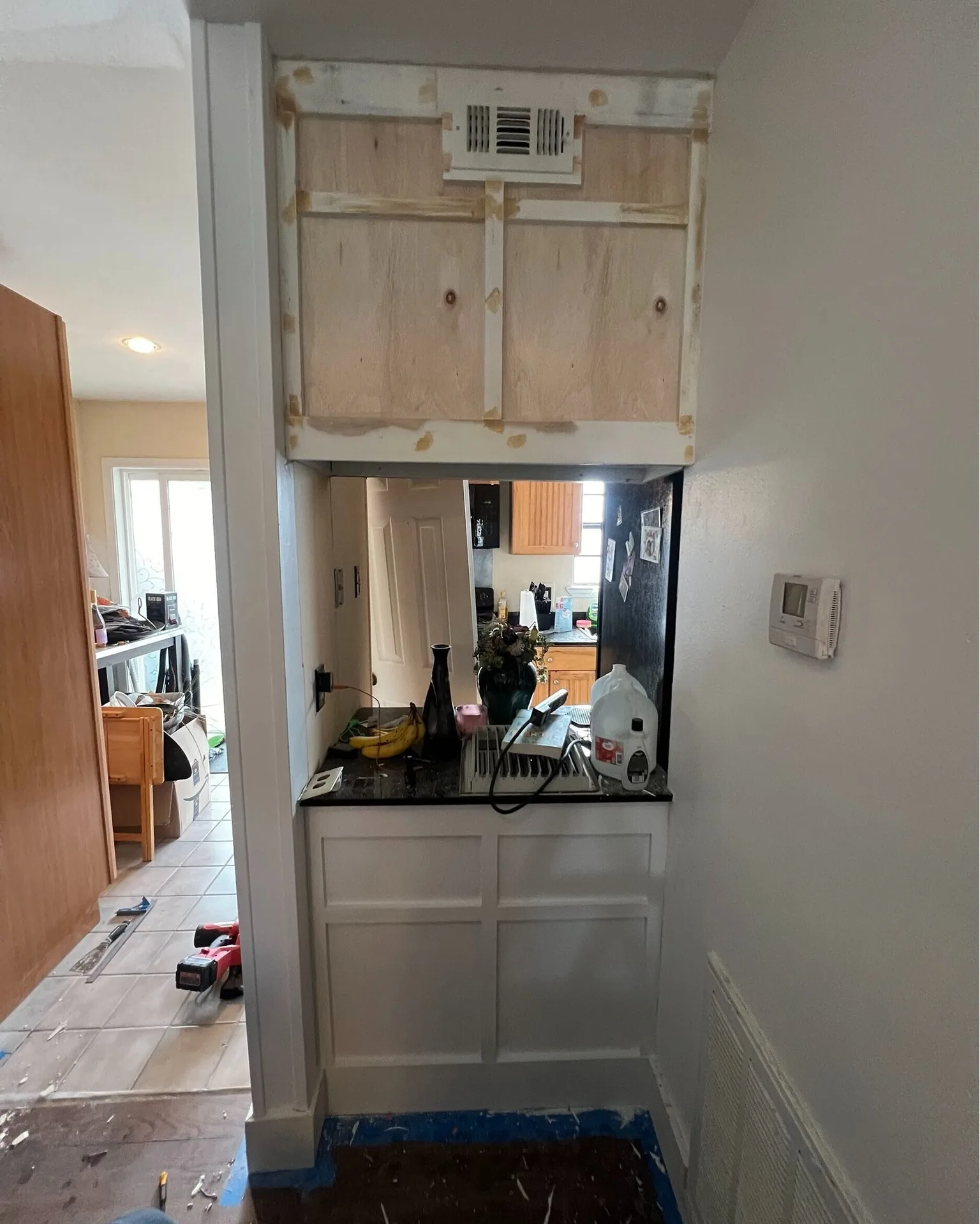 Gretna LA kitchen pass-through opening with overhead cabinet box exposed for refacing, raw plywood patches and HVAC vent visible above granite counter — mid-remodel framing work by Cajun Home Services