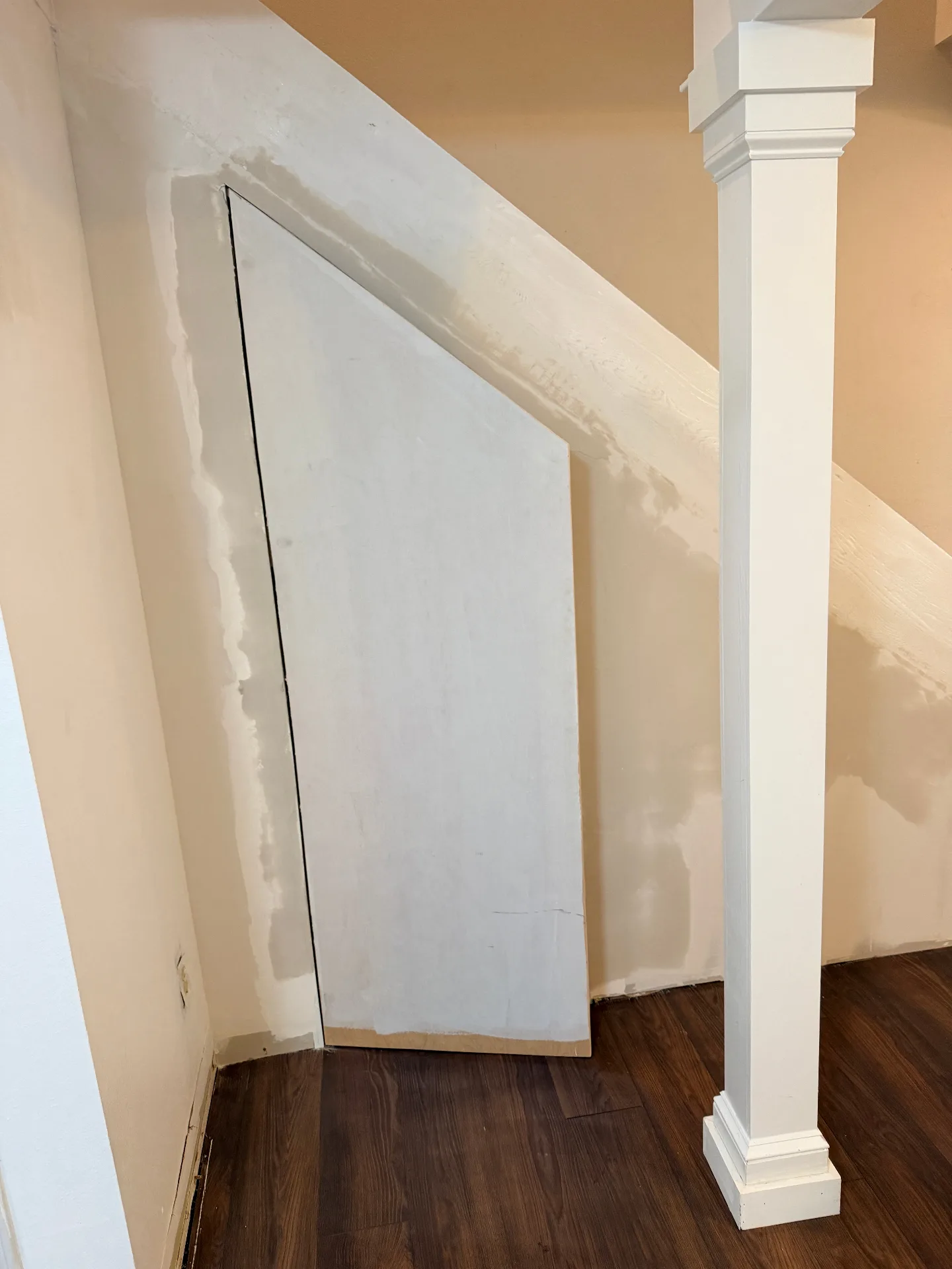 Gretna LA custom under-stair storage access panel cut into drywall and primed white, angled to follow stringer line beside newly installed column wrap and walnut LVP flooring by Cajun Home Services