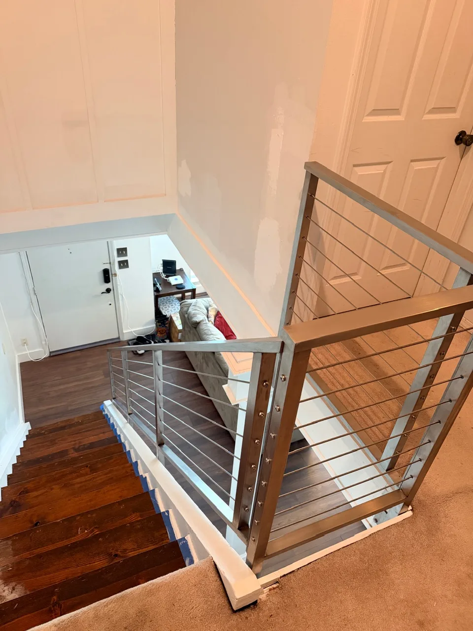 Gretna LA upper landing view down to refinished walnut staircase with new modern stainless steel cable railing system installed, board-and-batten feature wall visible across the open stairwell by Cajun Home Services