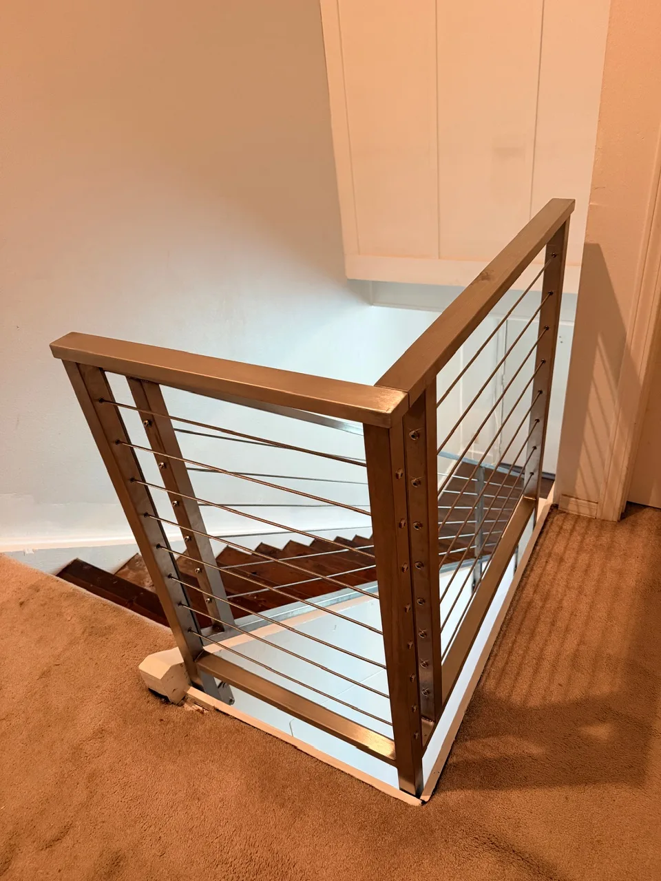 Gretna LA top-of-stair stainless steel cable railing detail showing brushed metal top rail, tensioned horizontal cables, and corner post anchored over freshly painted white base trim by Cajun Home Services