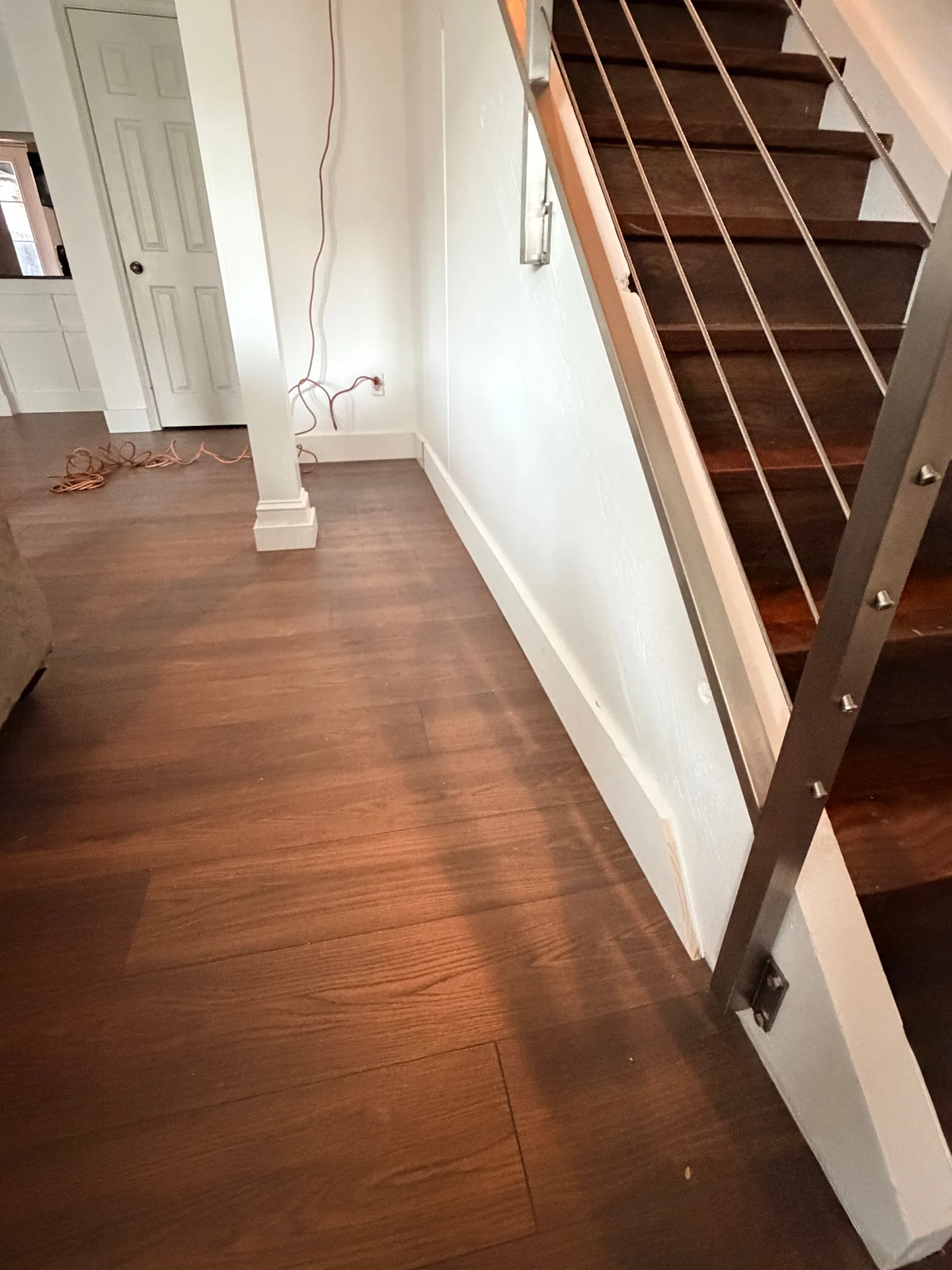 Gretna LA entryway with finished walnut LVP flooring flowing into stair landing, new white column wrap and stainless cable railing post anchored to freshly painted base trim by Cajun Home Services