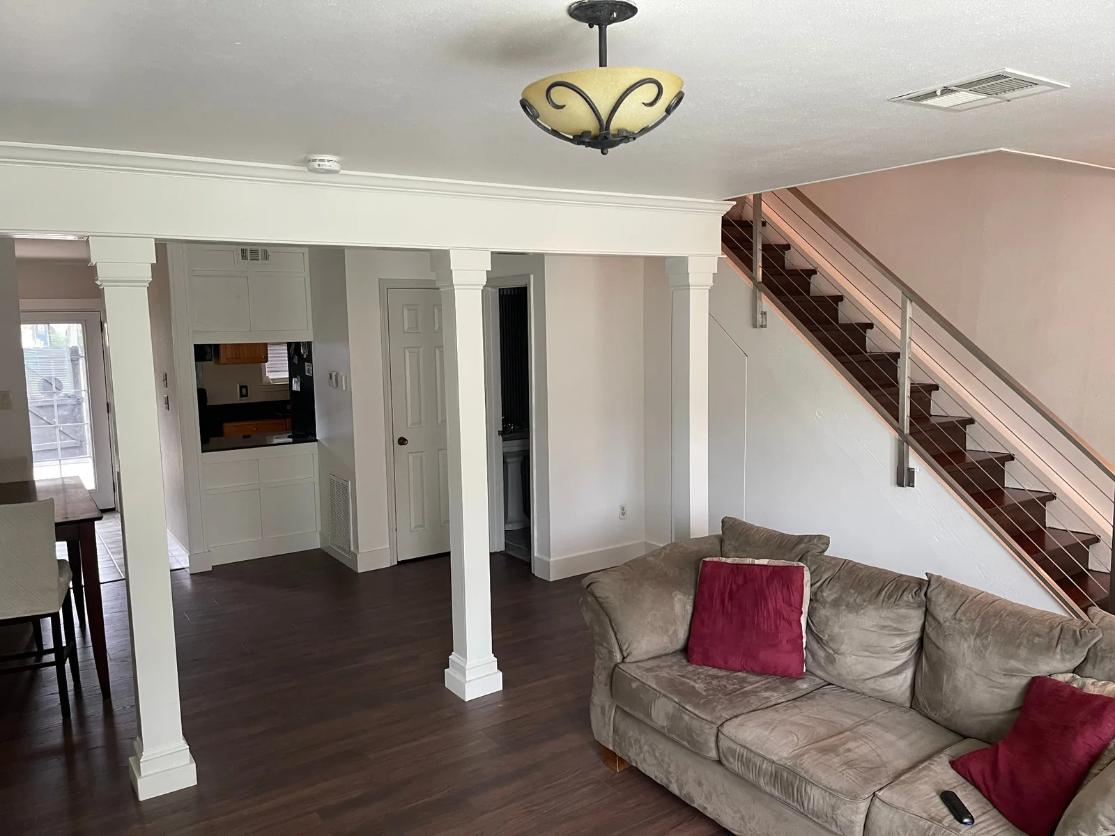 Gretna LA finished open-concept main floor with white craftsman column wraps framing the kitchen pass-through, refinished walnut staircase with stainless cable railing, and walnut LVP flooring throughout by Cajun Home Services