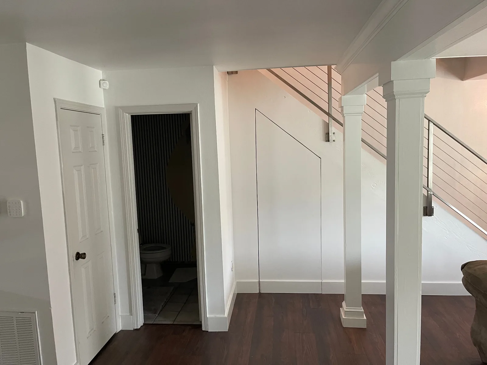Gretna LA finished entry hallway with custom under-stair angled access panel painted flush white, half-bath doorway and craftsman column wraps anchoring the stainless cable railing staircase by Cajun Home Services