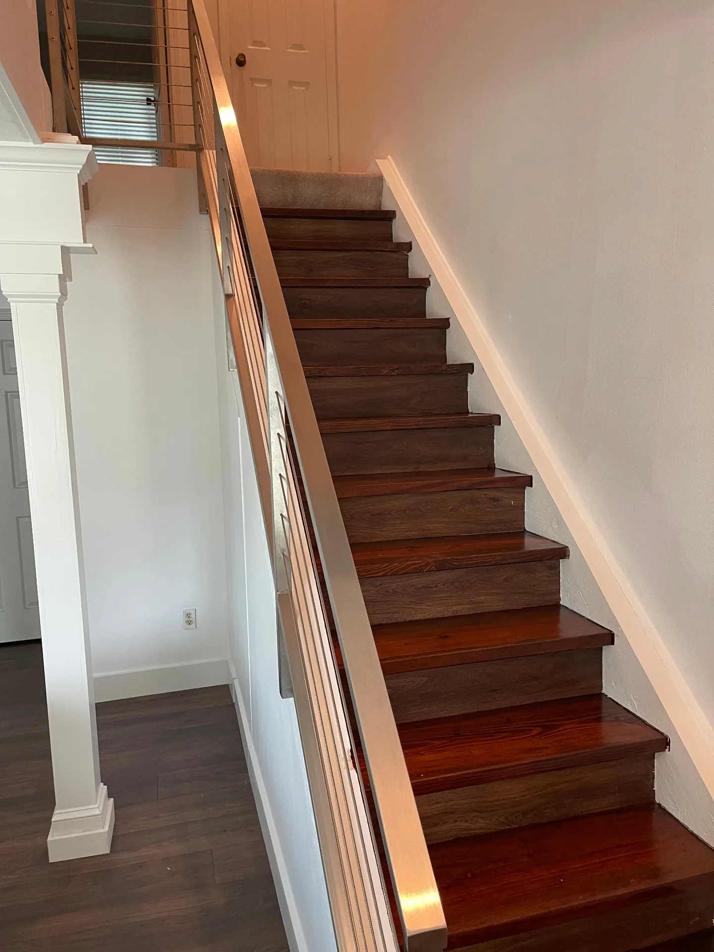 Gretna LA finished staircase with dark walnut stained treads, crisp white risers, and brushed stainless cable railing running up beside freshly wrapped craftsman column details by Cajun Home Services
