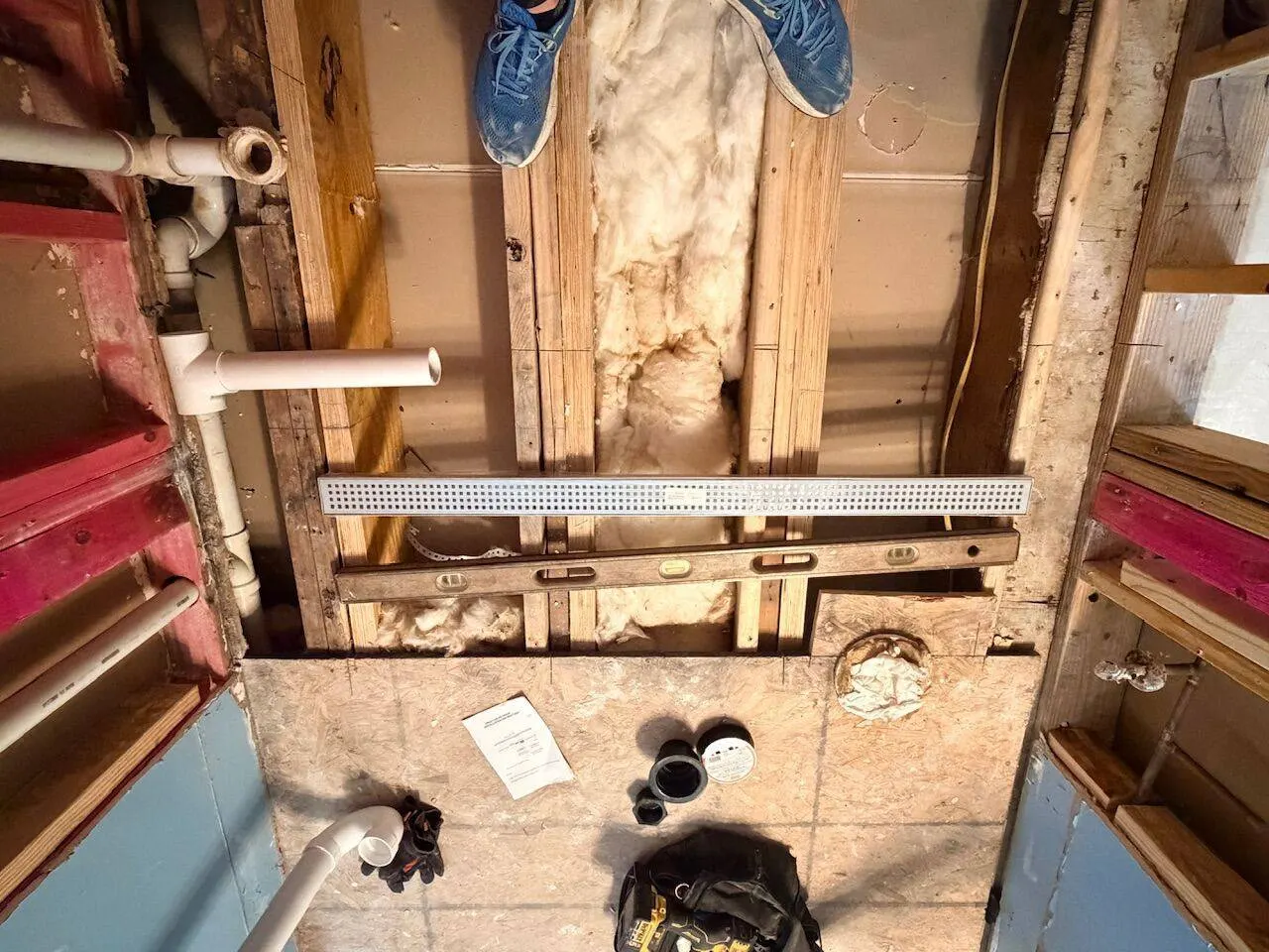 Overhead view of bathroom demolition with exposed framing insulation and plumbing rough-in during renovation