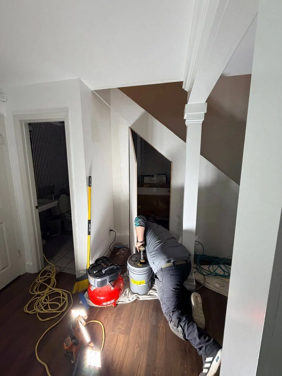 Crew member building custom under-stair closet with air compressor and work lights during renovation