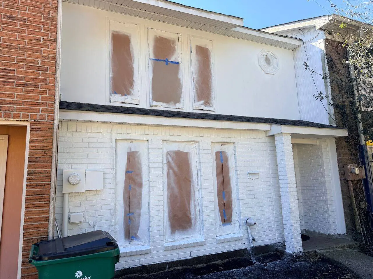 Exterior brick painting preparation with windows masked during make-ready service in Metairie