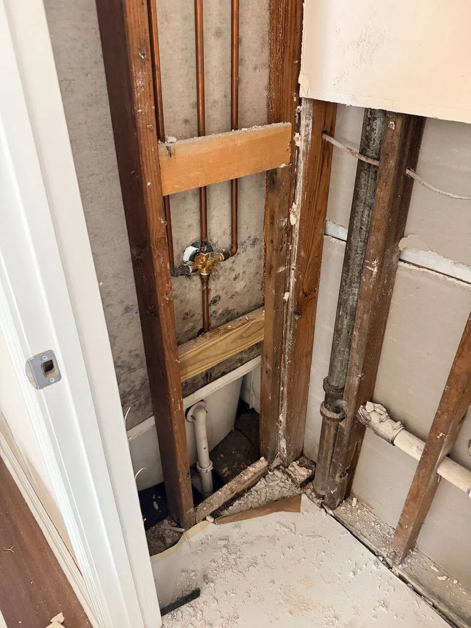 Plumbing rough-in with copper pipes and wall framing exposed during structural bathroom renovation
