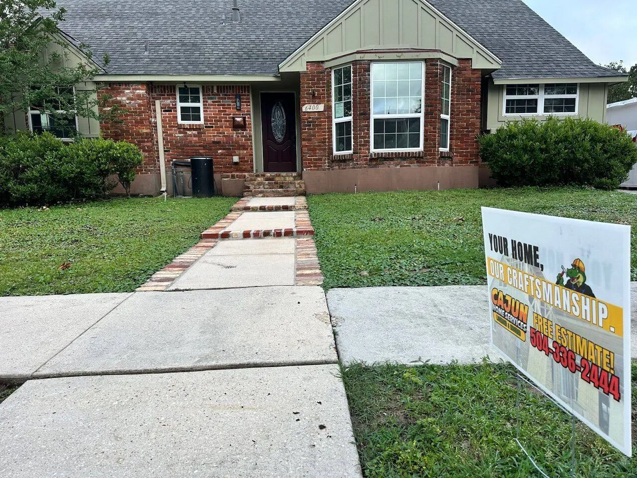 Completed shingle roof on brick home with Cajun Home Services yard sign showing free estimate phone number