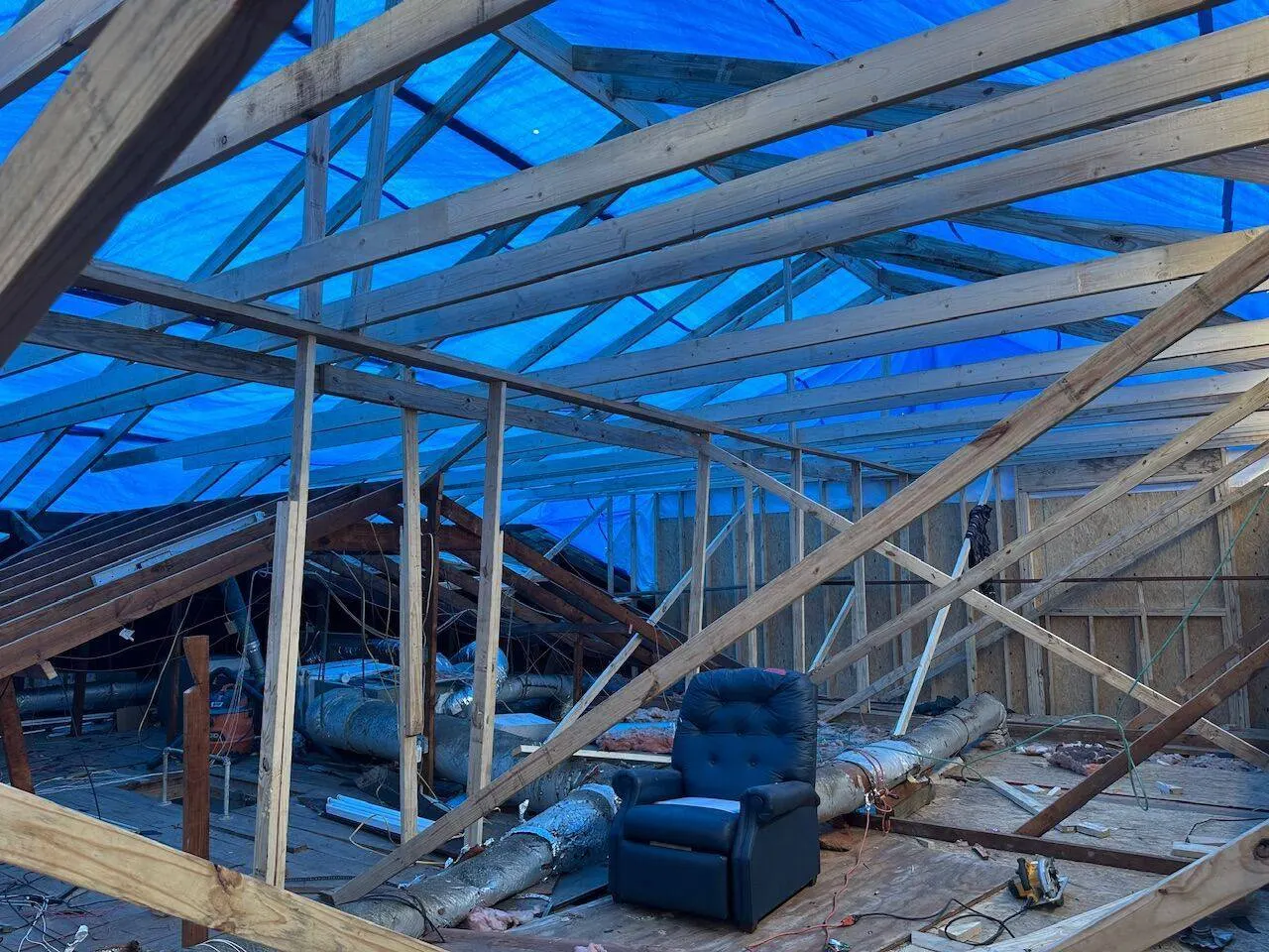 Interior roof framing with blue tarp overhead during full structural rebuild showing rafters and ductwork