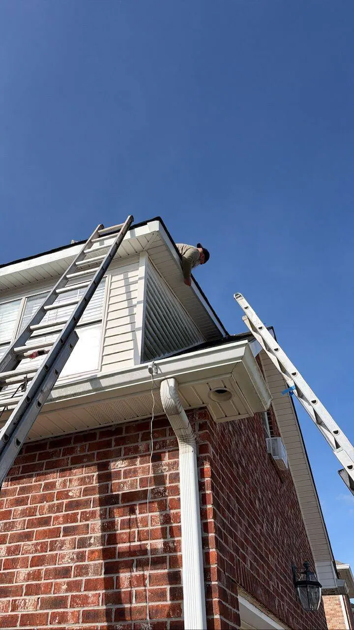Roofing crew member working on fascia and drip edge at roof peak on brick home in Southeast Louisiana