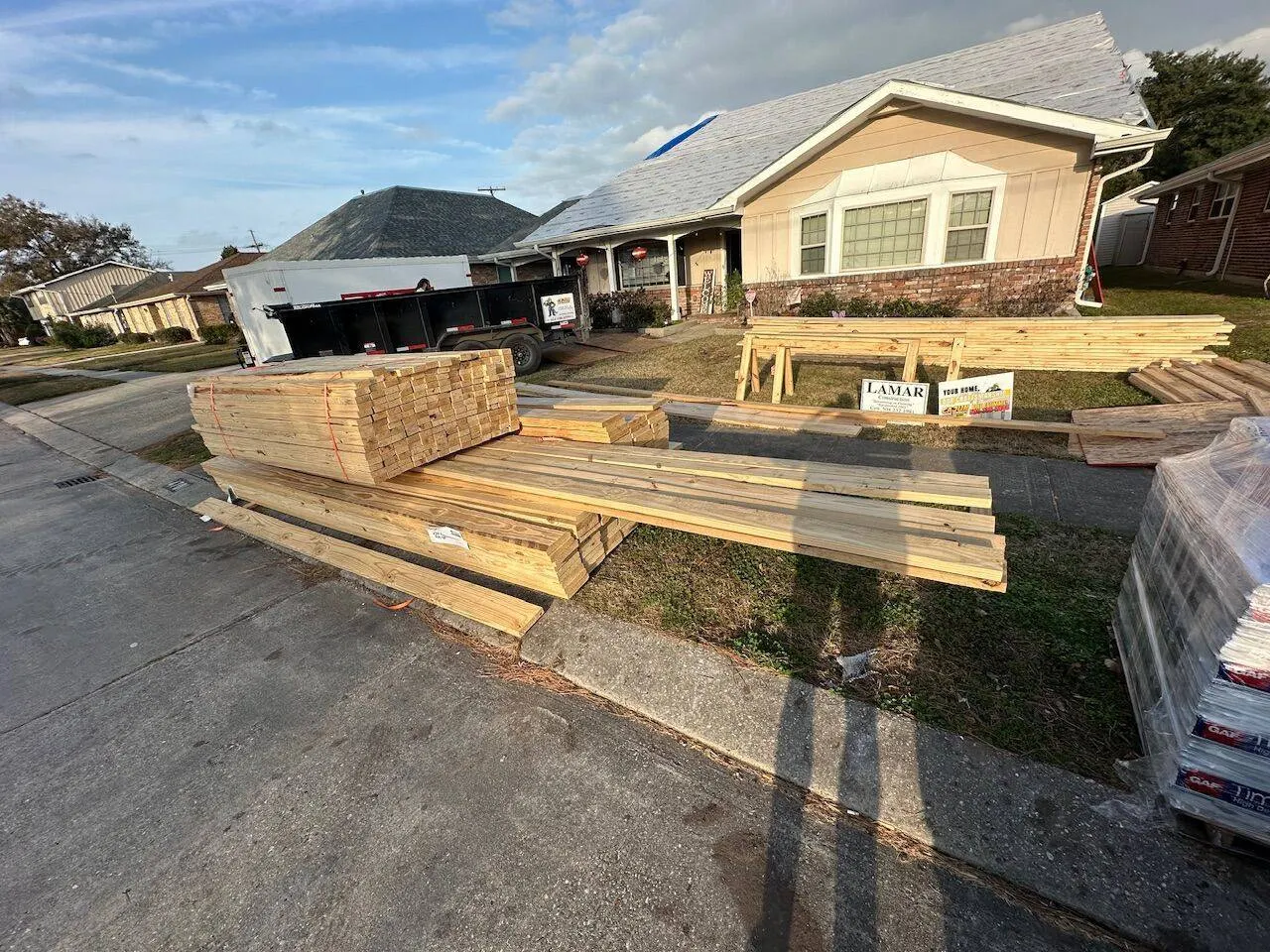 Lumber and GAF shingle pallets delivered to active roofing jobsite with Cajun Home Services trailer in Metairie
