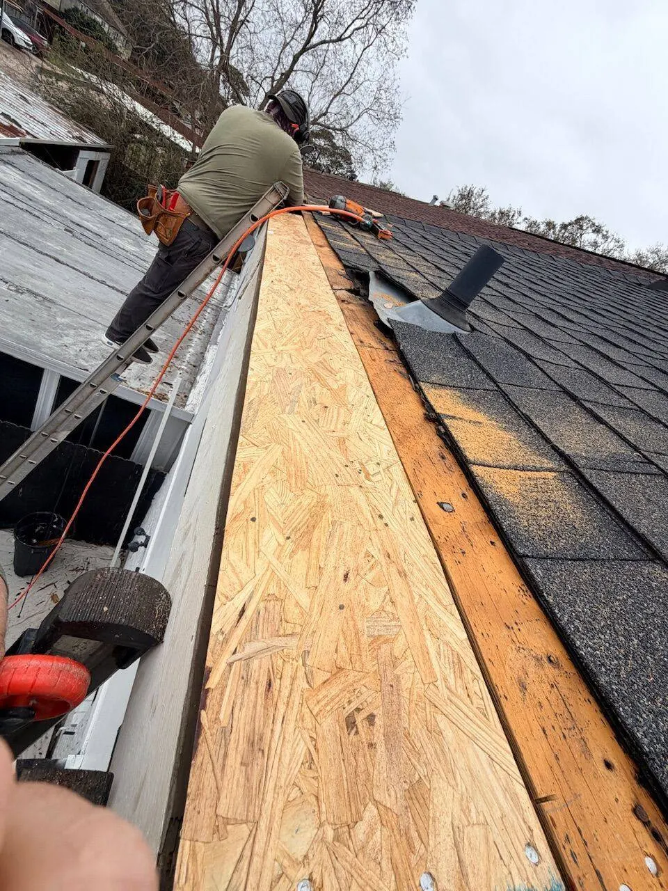Crew installing OSB sheathing along roof edge with shingles partially installed on Louisiana residential roof