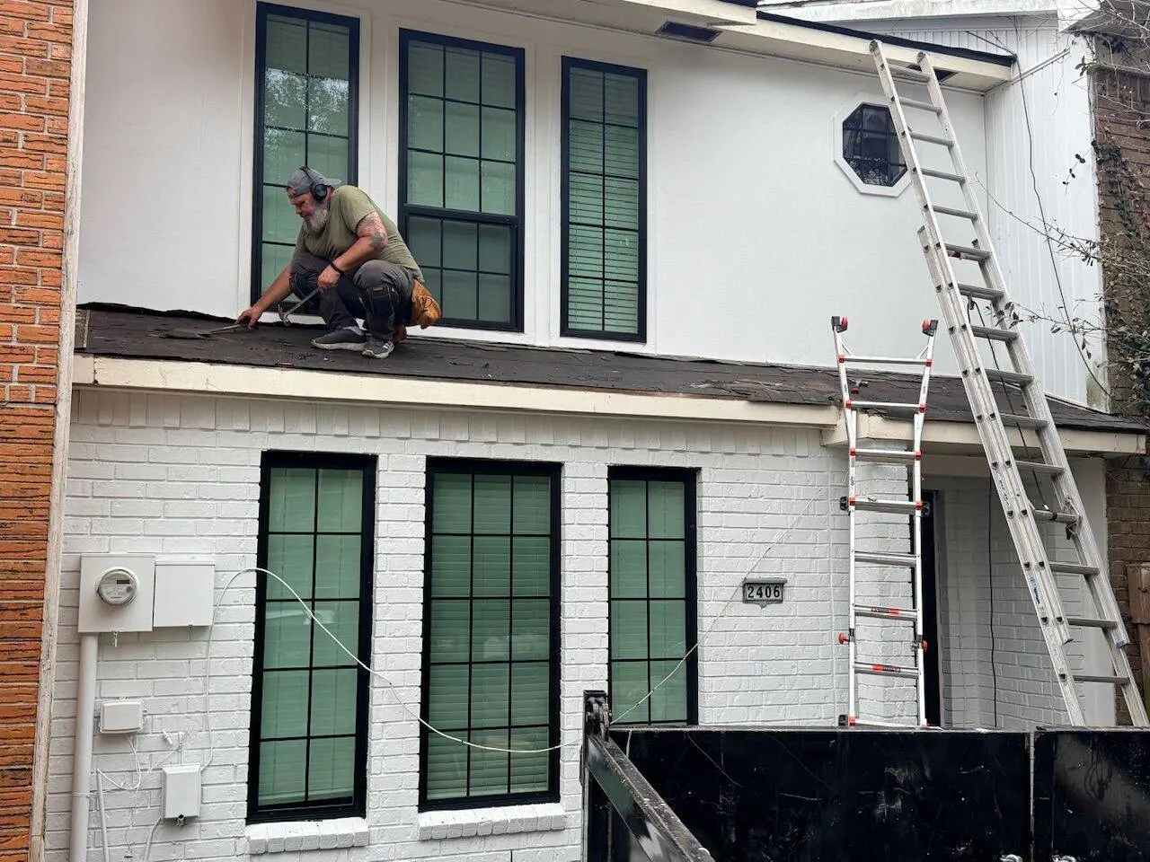 Roof tearoff in progress on white brick townhome with crew removing old shingles in New Orleans area