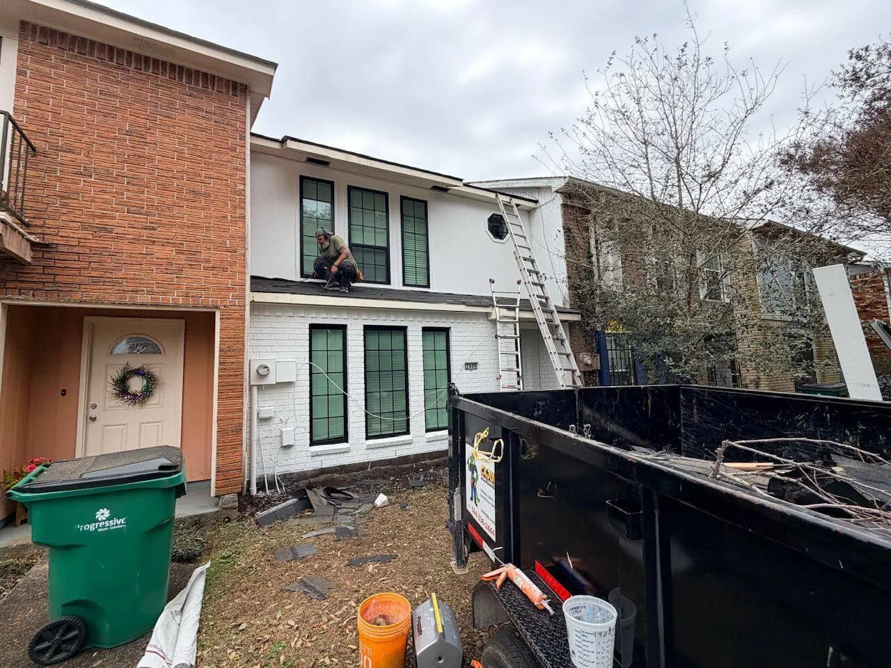 Active roofing jobsite with dump trailer and crew working on townhome roof replacement in New Orleans