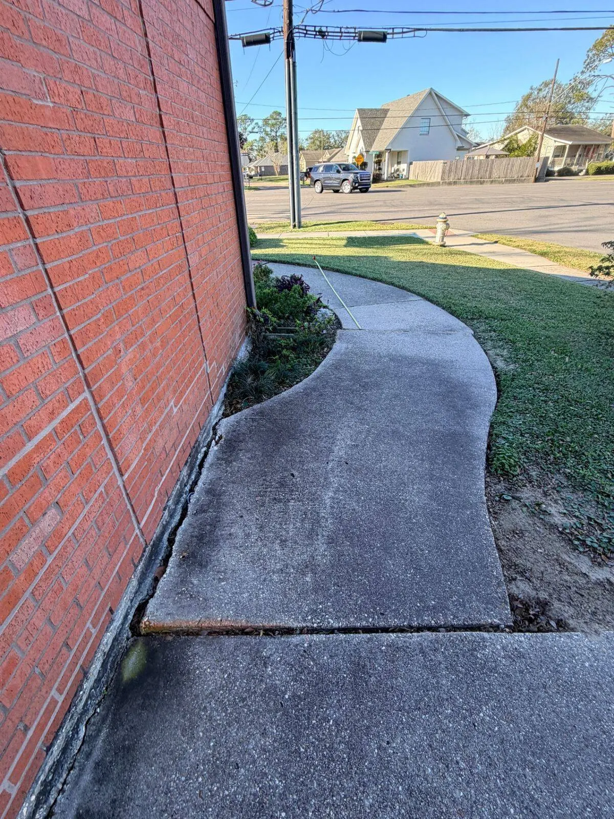 Curved sidewalk uplifted by invasive tree roots before replacement along Jefferson Highway commercial facility in Jefferson Parish Louisiana