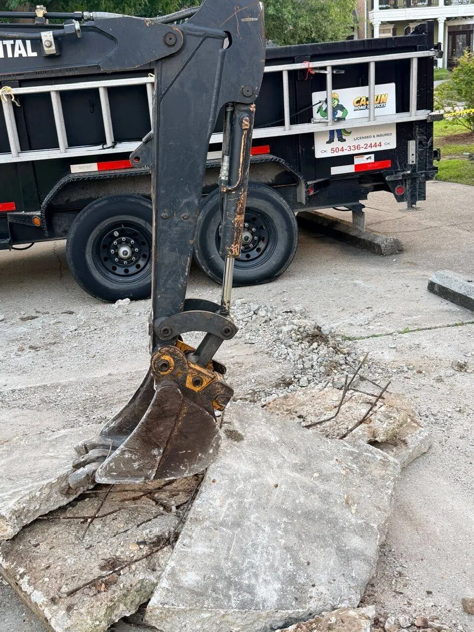 Mini excavator breaking apart rebar reinforced concrete during Jefferson Highway sidewalk demolition in Jefferson Parish Louisiana